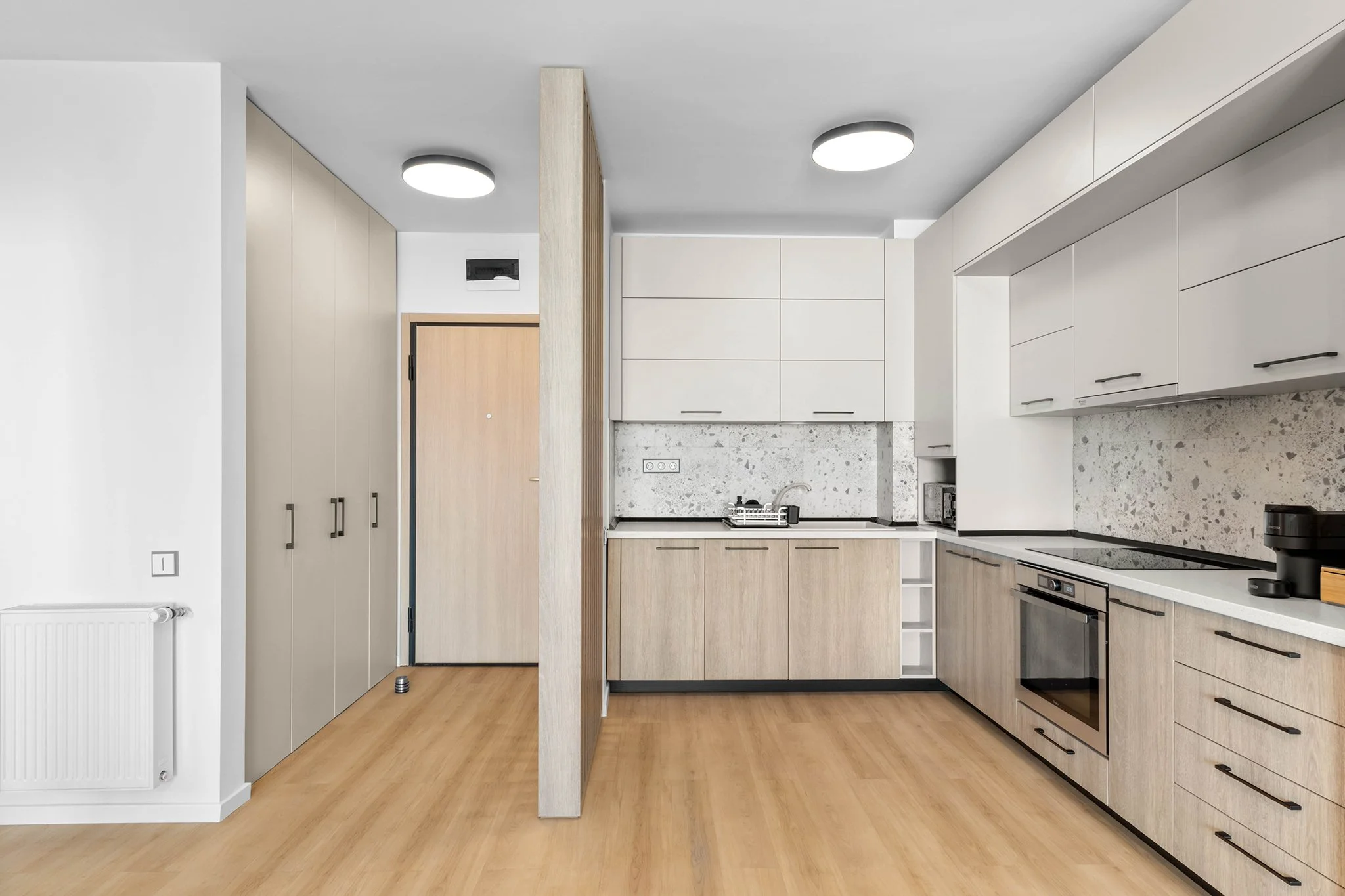 Modern kitchen interior with light wooden cabinets, built-in oven, tile backsplash, and wooden flooring.