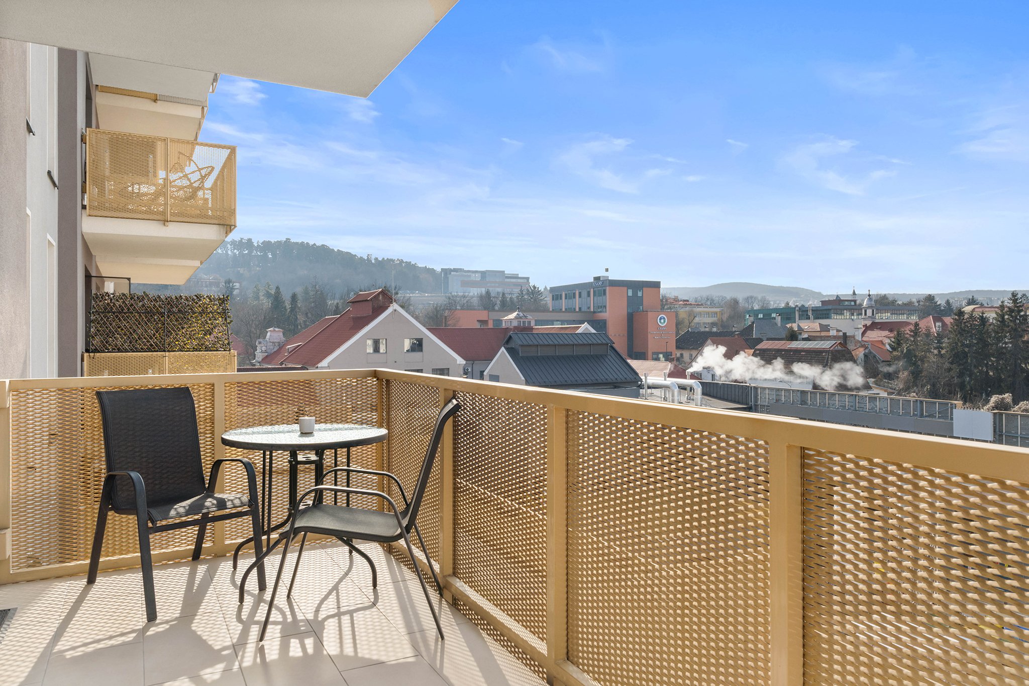 Apartment balcony with table and chairs, overlooking town buildings and hills
