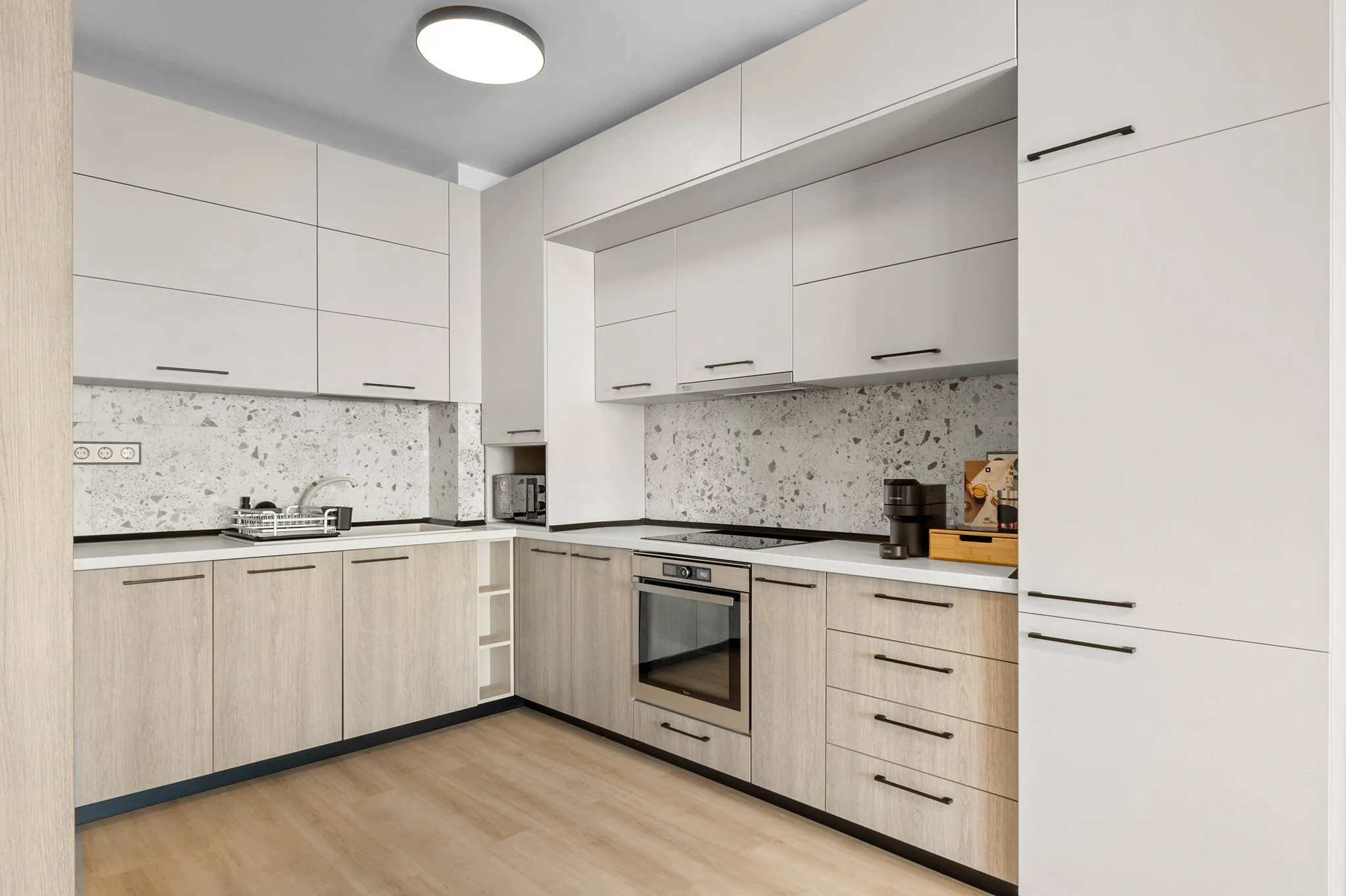 Modern kitchen with sleek cabinetry, built-in oven, stovetop, coffee maker, and light wood flooring.
