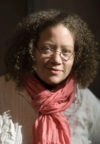 Person with curly hair, wearing glasses, a white shirt, and a coral scarf.