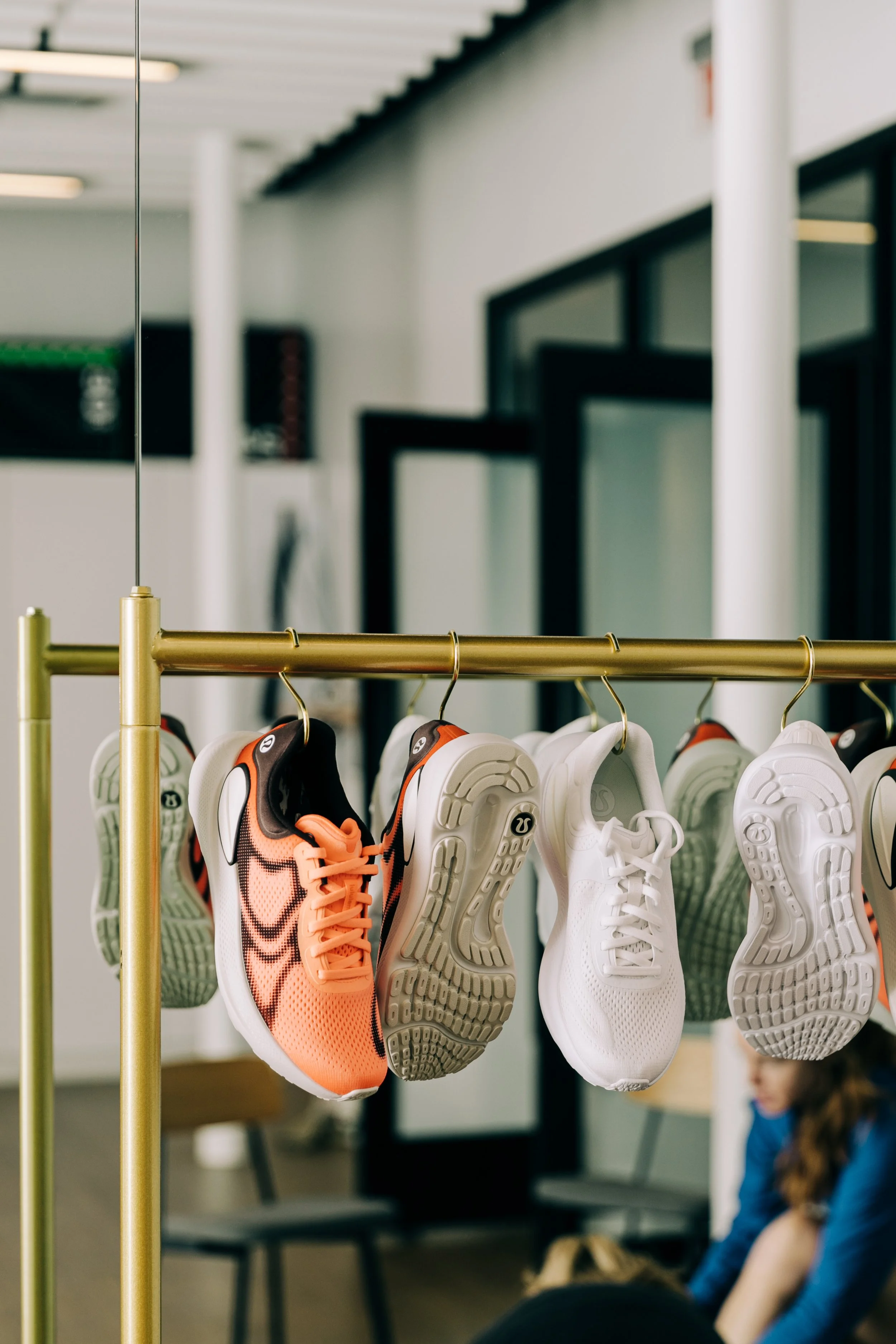 Bright orange and white athletic shoes hanging on a gold clothing rack in a sports store or gym.