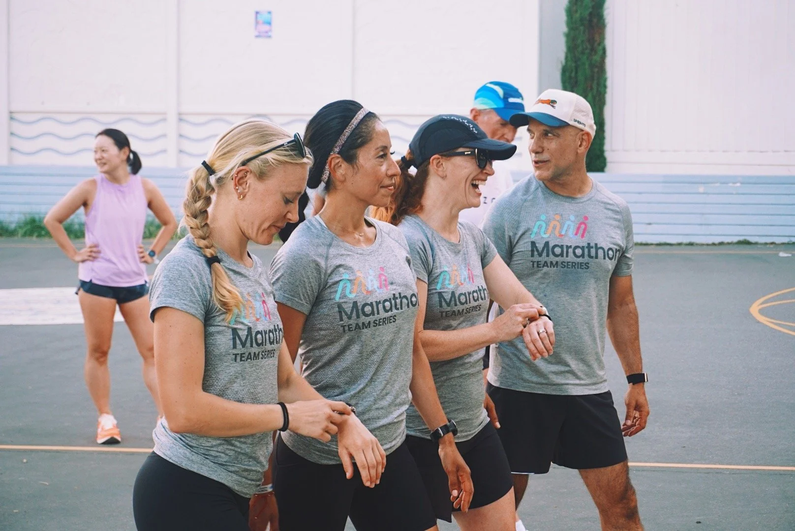 Group of runners, wearing gray marathon team T-shirts, walking and talking on an outdoor track.