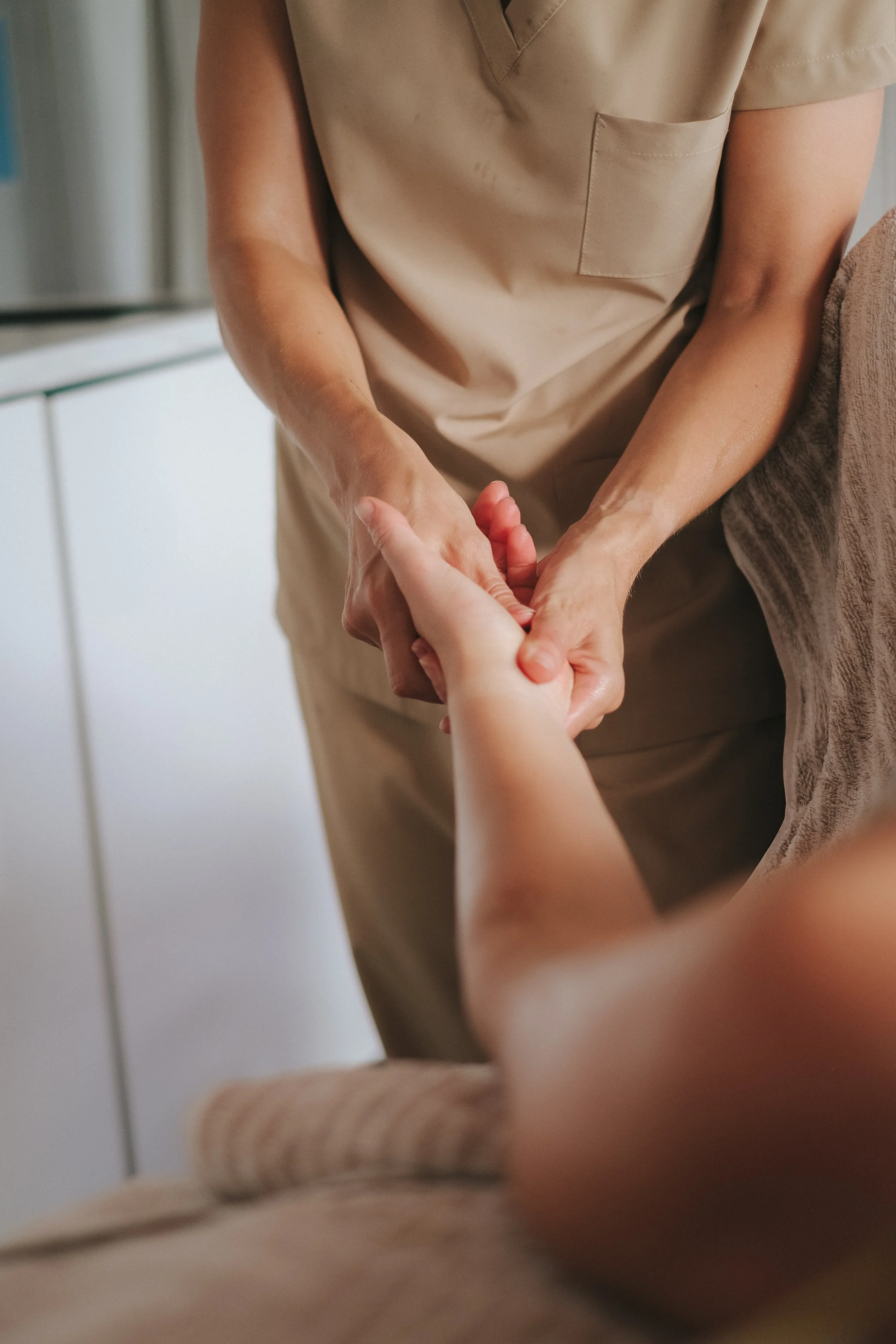 A woman in beige scrubs massaging another person's hand during a facial.