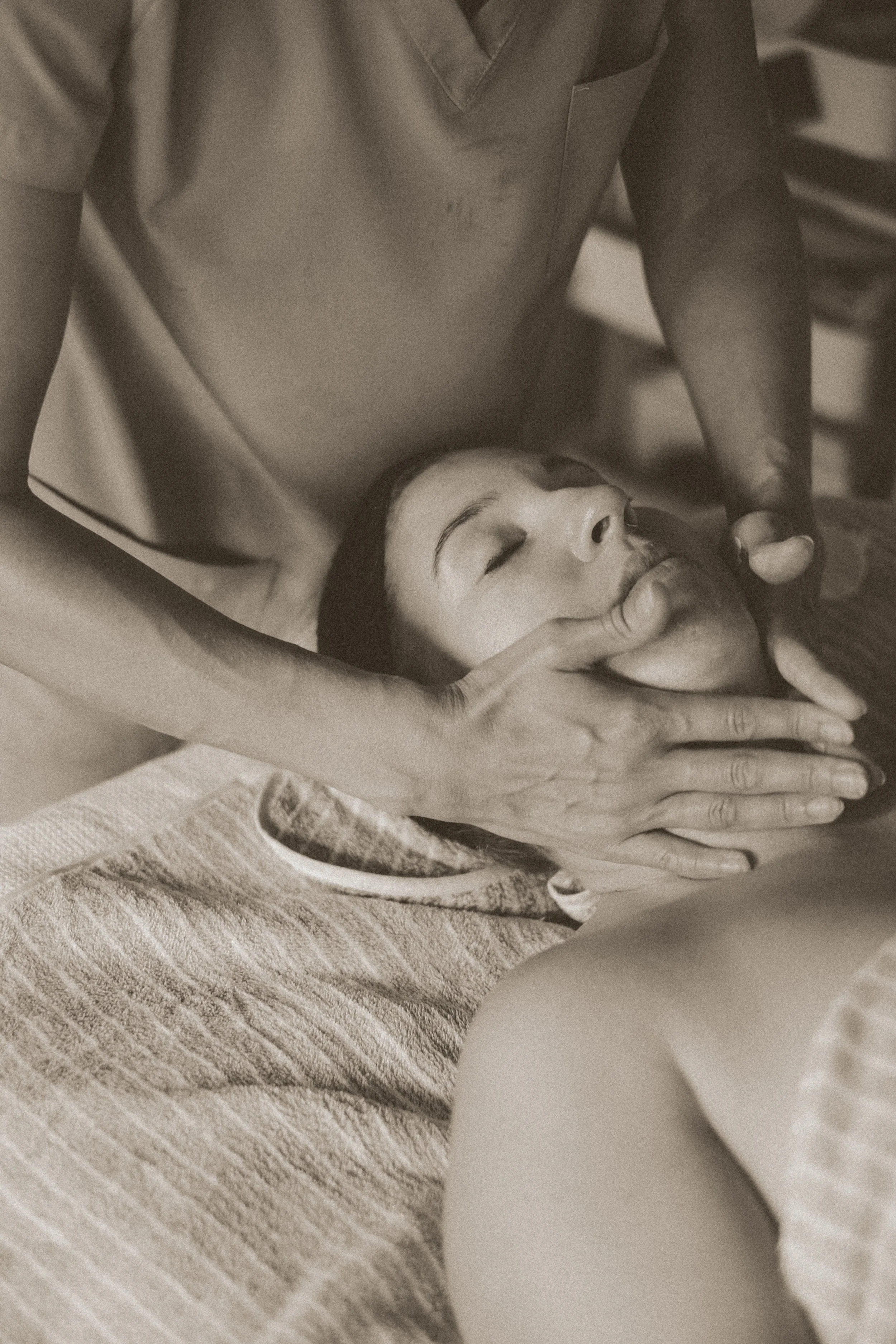 A woman receives a facial massage in a spa setting, lying down with her eyes closed and relaxed.