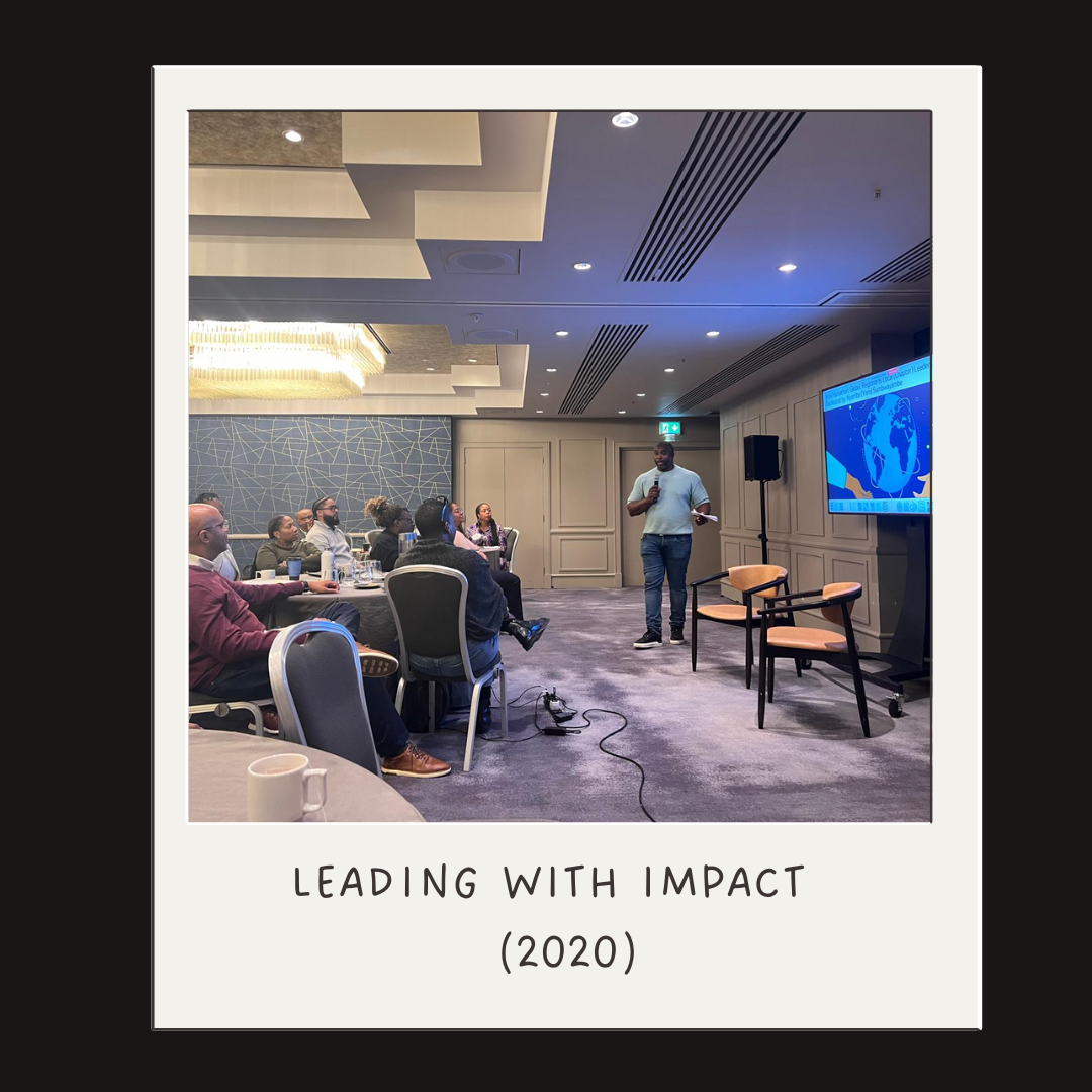 A man giving a presentation to an audience seated at round tables in a conference room with a large screen displaying a globe behind him. Caption: 'Leading with Impact (2020).'