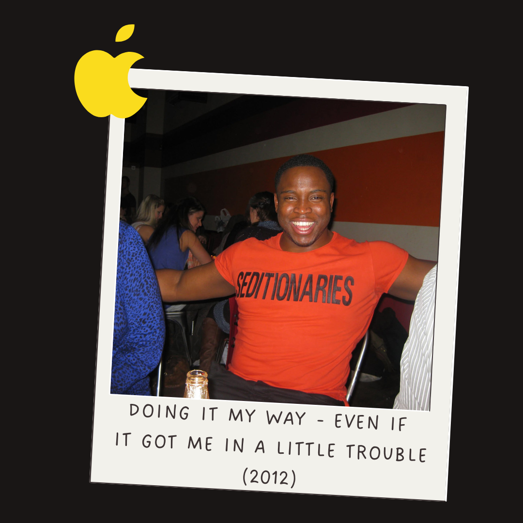 A smiling man wearing an orange T-shirt with the word 'Seditionaries' printed on it, sitting at a table in a crowded room, with a caption below that reads 'Doing it my way - even if it got me in a little trouble (2012).'