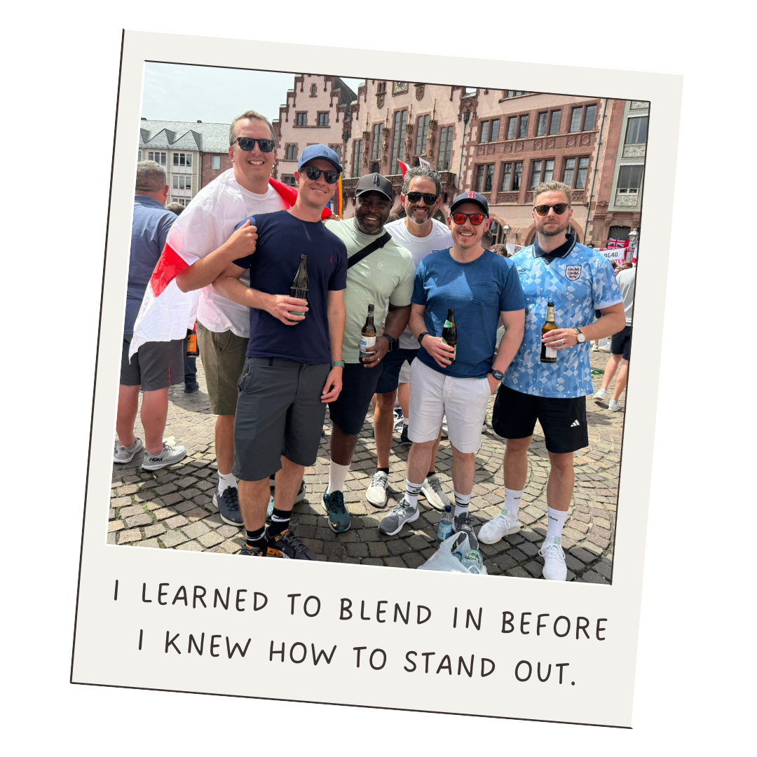 A group of six young men standing together outdoors in a European city square, smiling and holding beers, with historical buildings in the background. The photo has a caption saying, "I learned to blend in before I knew how to stand out."