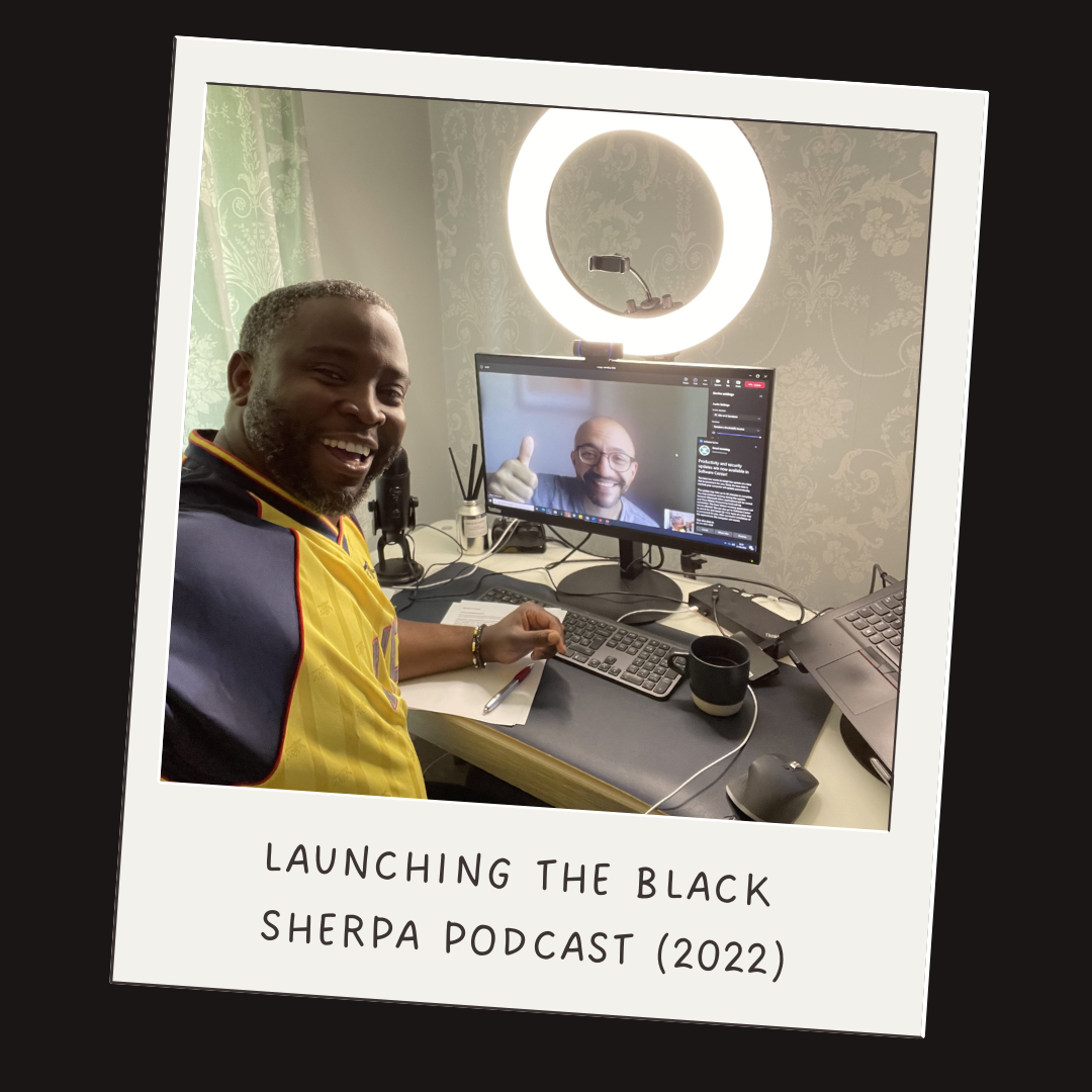 Two men in a home office, one sitting at a desk with a computer and the other on a computer screen smiling and giving a thumbs-up. Text overlay reads 'Launching the Black Sherpa Podcast (2022).'