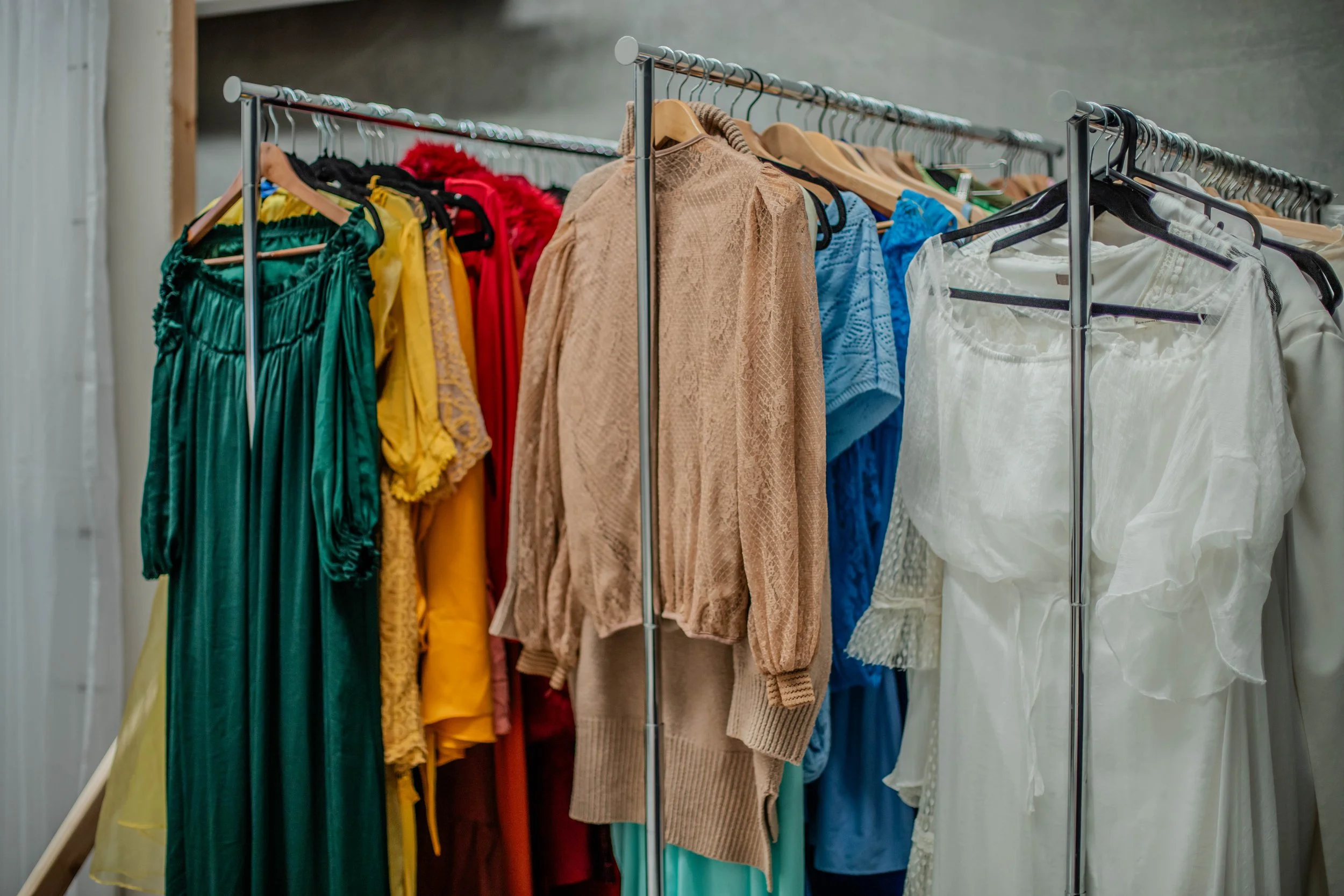 Clothing rack holding various colorful dresses, skirts, and tops on hangers.