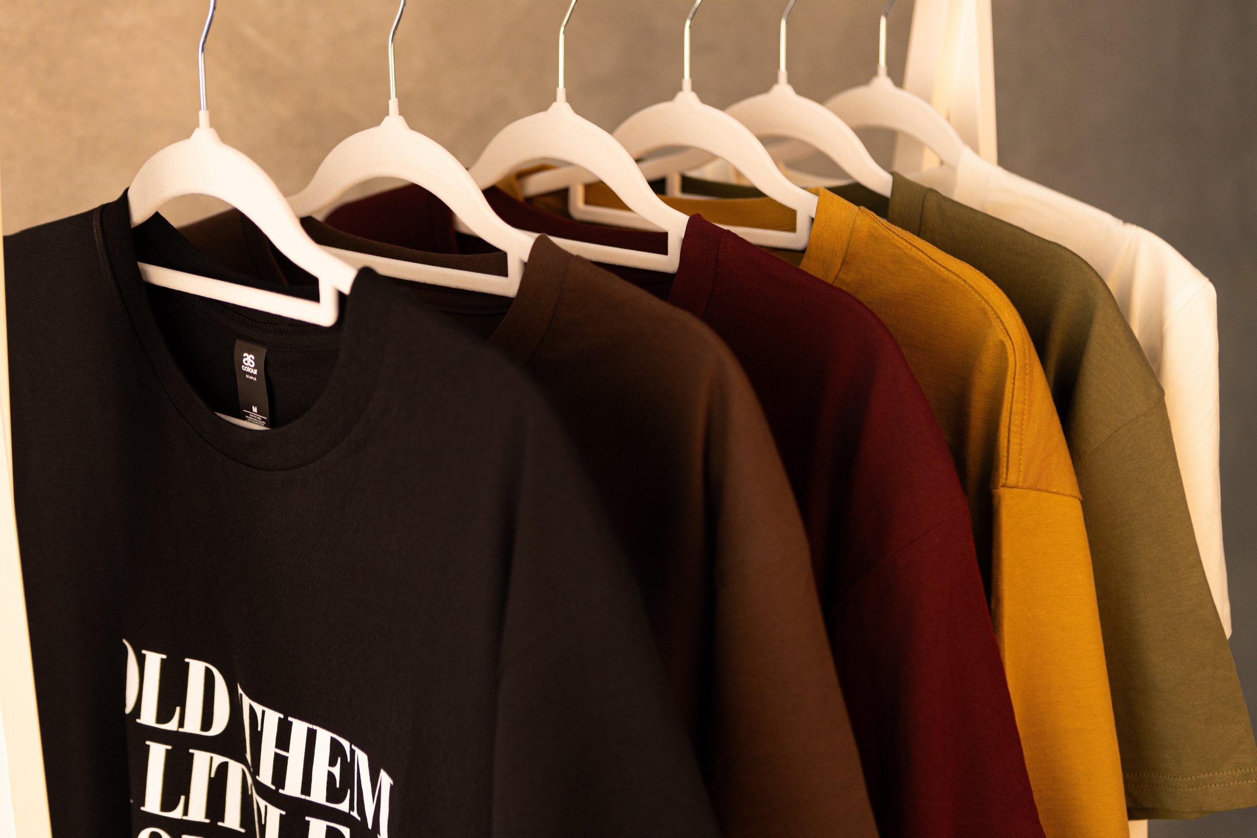 An assortment of T-shirts hanging on white hangers, arranged by color from black to white.