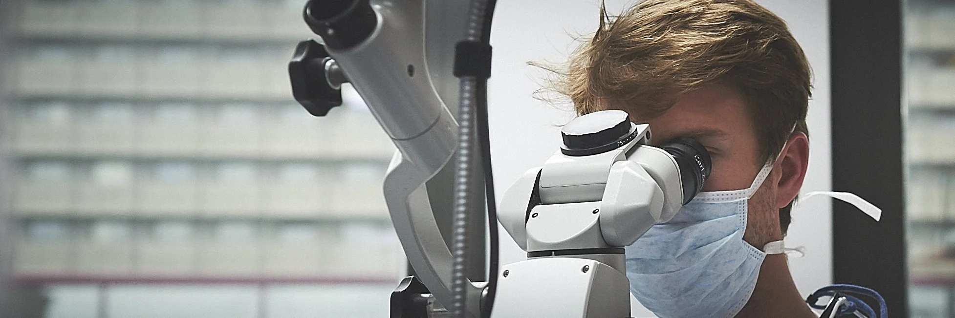 Personne portant un masque, utilisant un microscope médical.