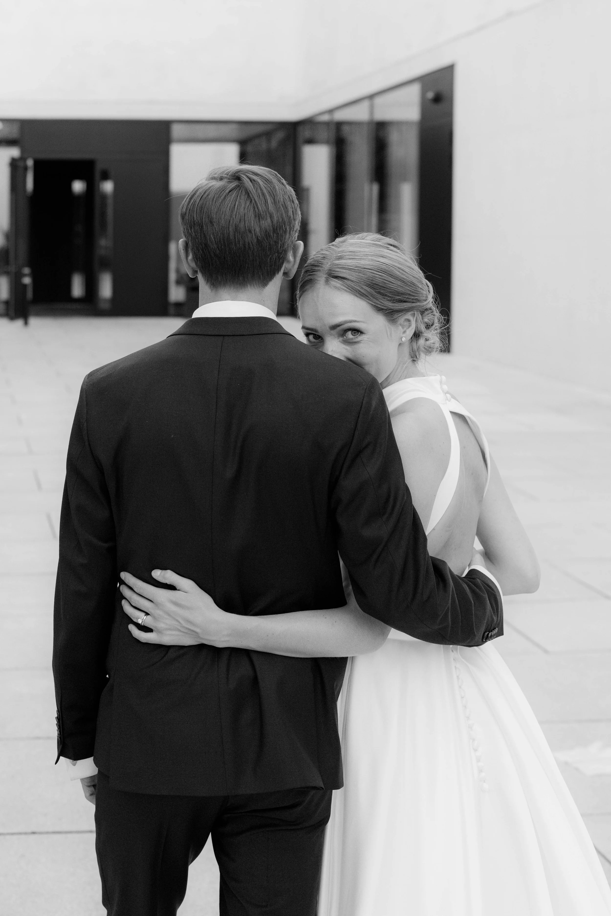 Ein Brautpaar umarmt sich, das Mädchen blickt über die Schulter des Mannes und lächelt.