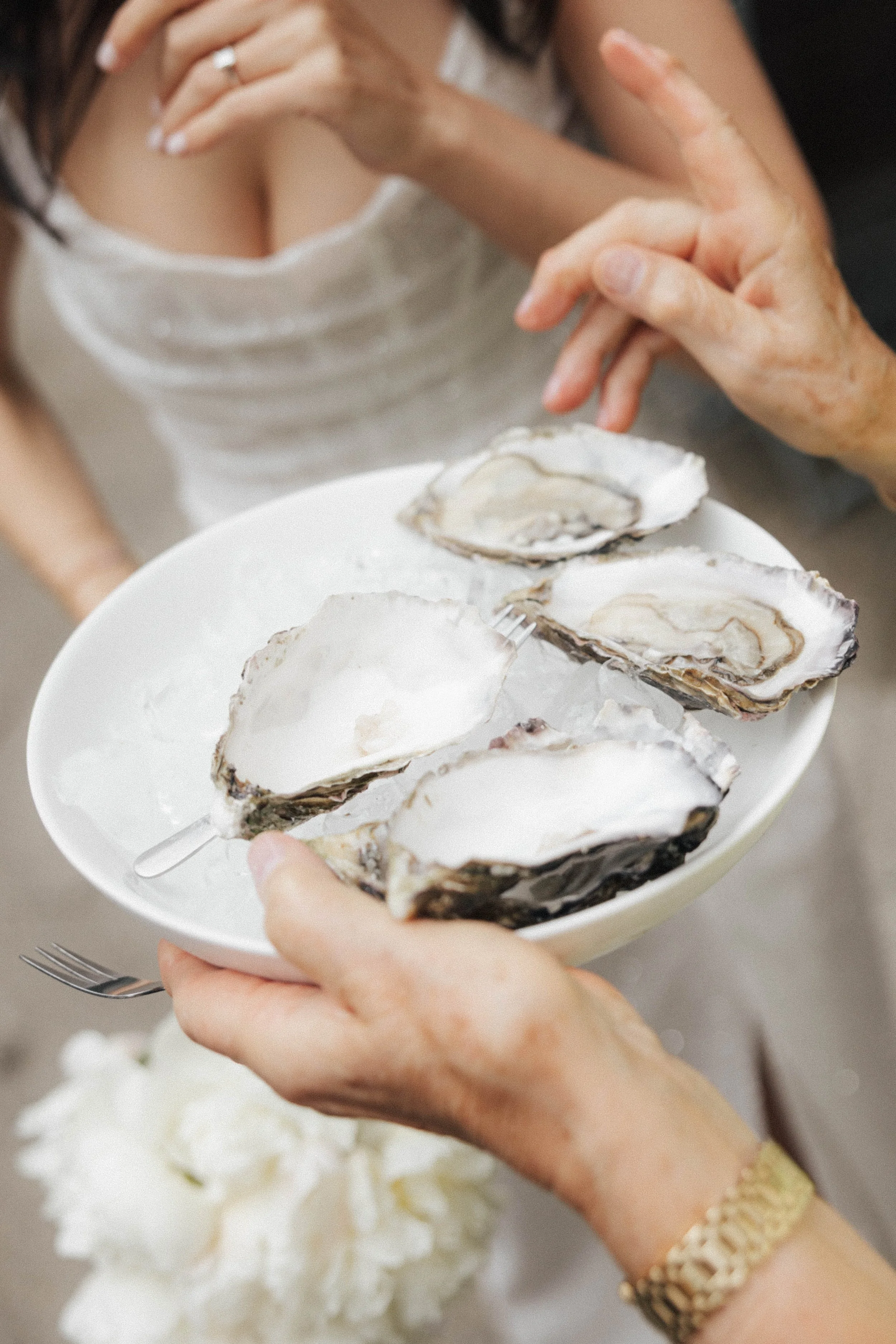 Oysters auf einem weißen Teller, geöffnet und bereit zum Verzehr, nahe bei einem weißen Blumensträu.