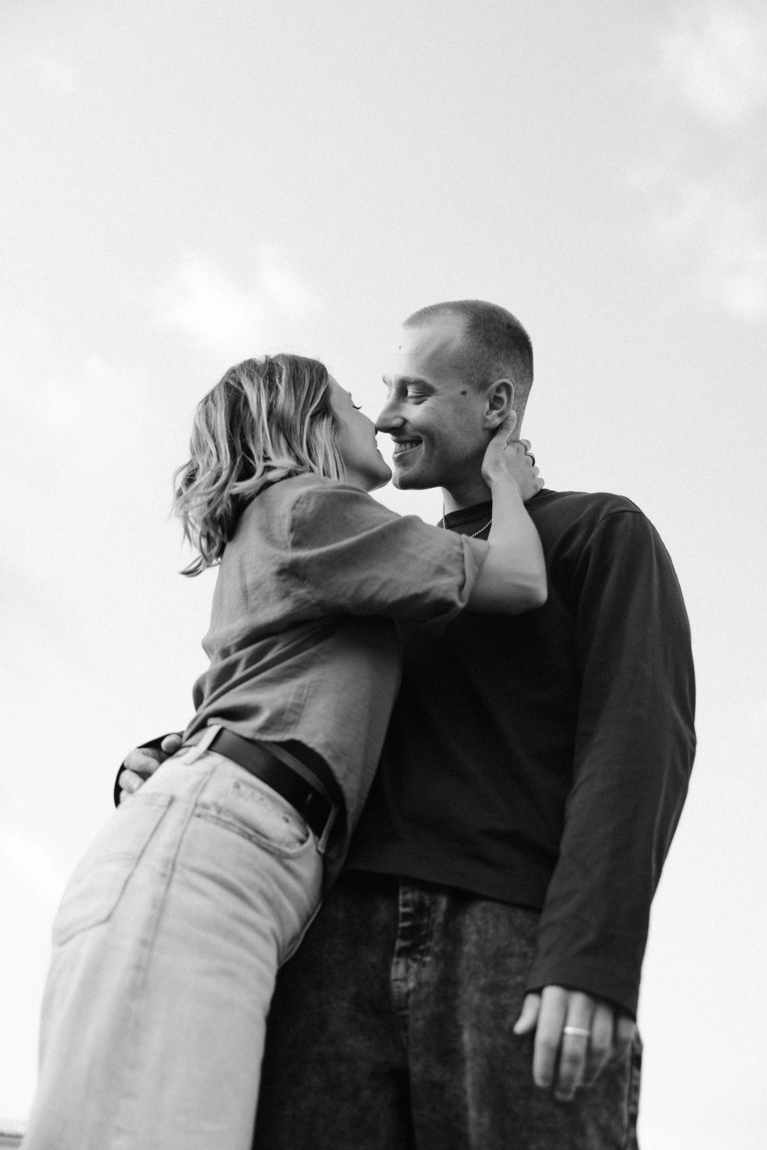Ein lächelndes Paar, das sich umarmt und küsst, in Schwarz-Weiß-Fotografie gegossen, bei goldener Stunde