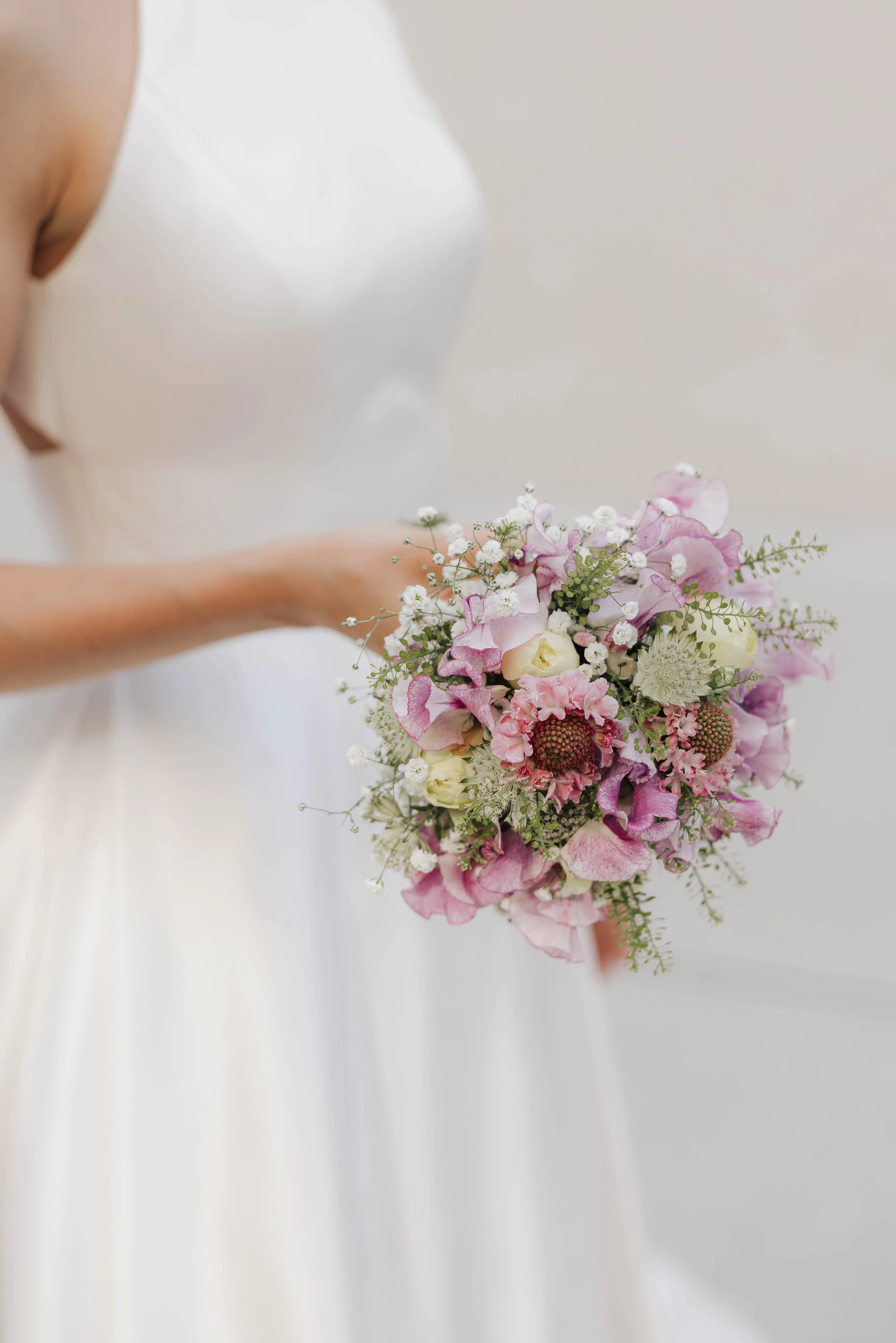 Braut hält einen Blumenstrauß mit rosa, weißen und grünen Blumen in einem weißen Kleid.