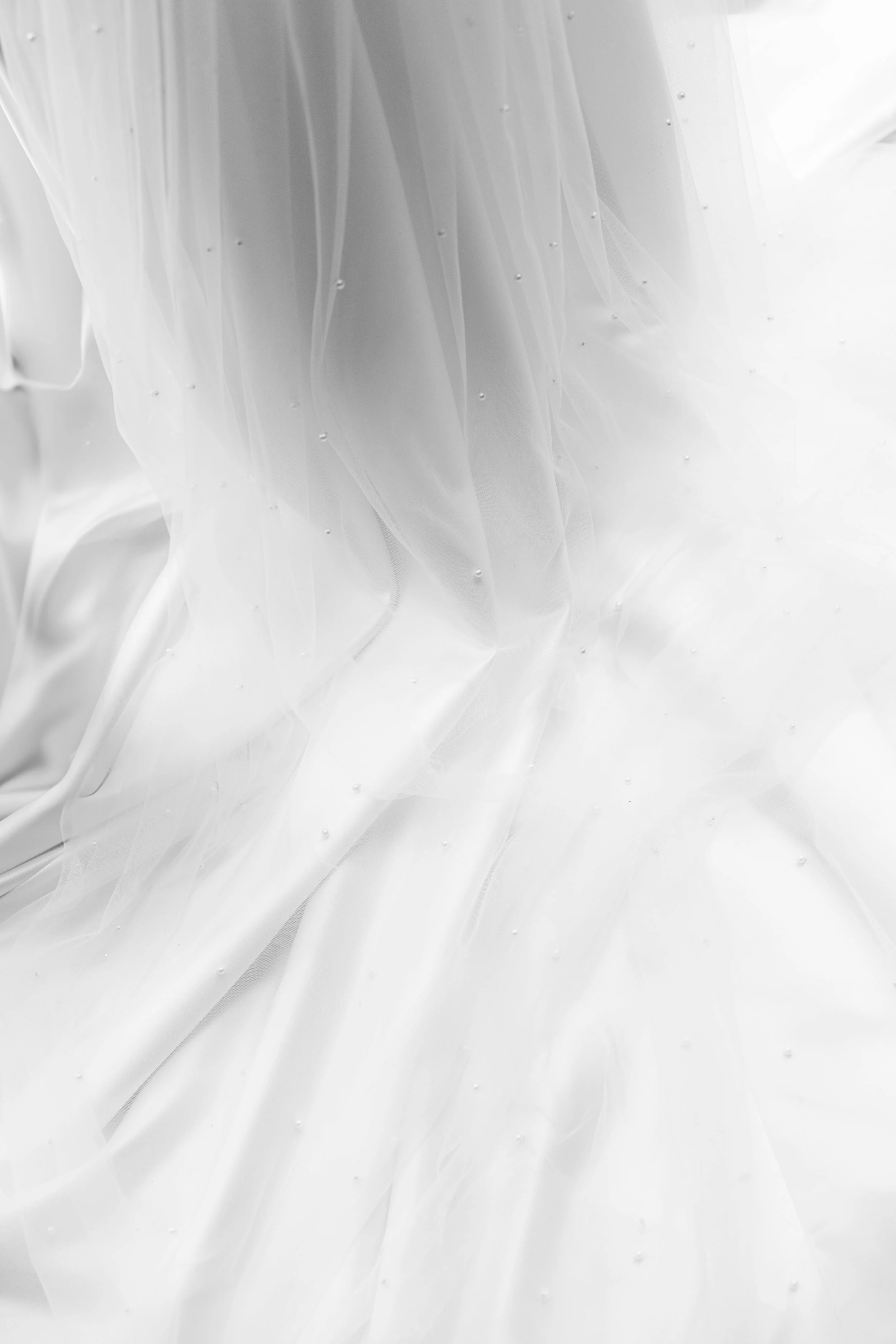 Nahaufnahme eines weißen Brautkleids mit Perlendetails und transparentem Tüllstoff.