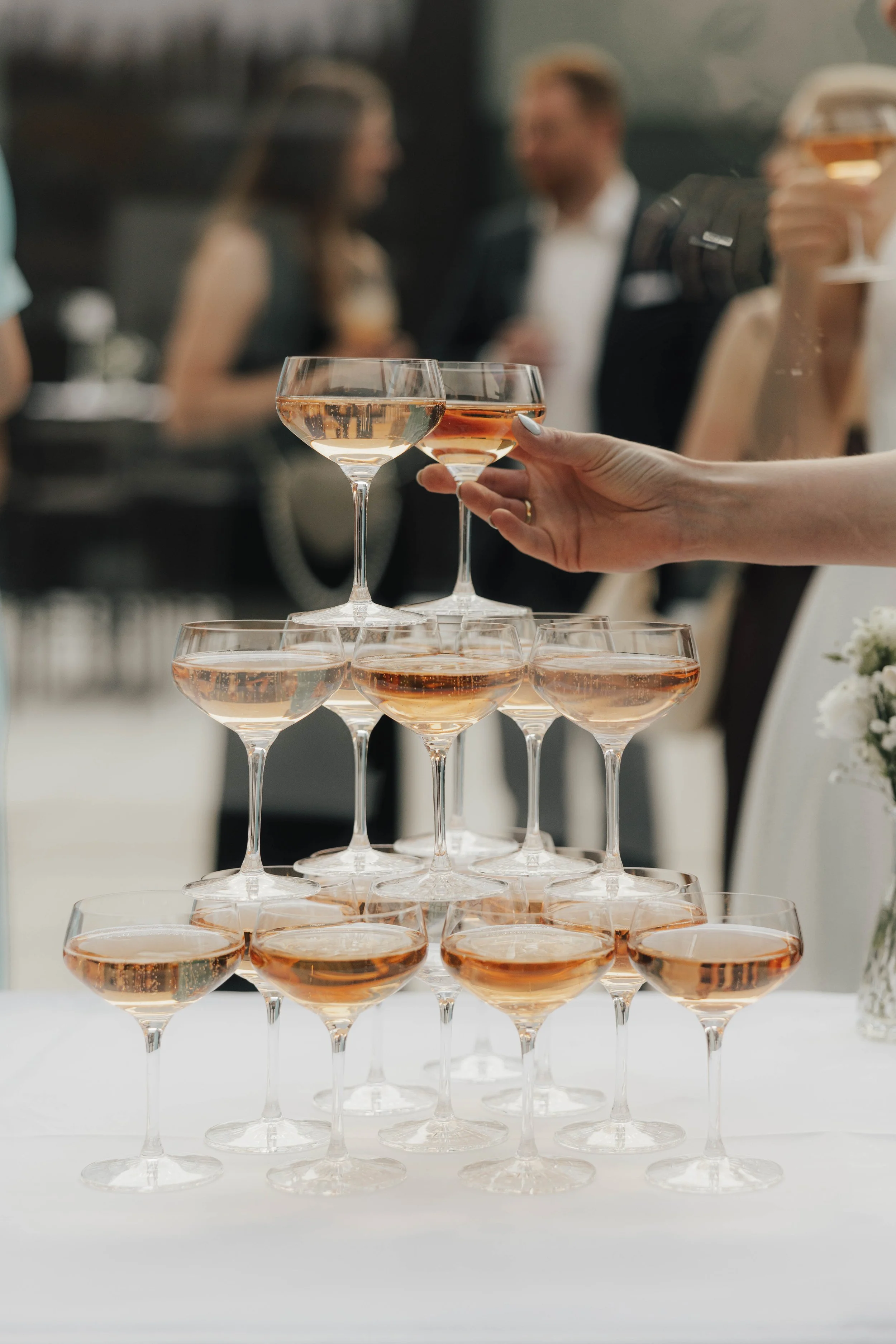 Tropfende Weinkelche auf einem Hochzeitstisch, mit Gästen im Hintergrund.