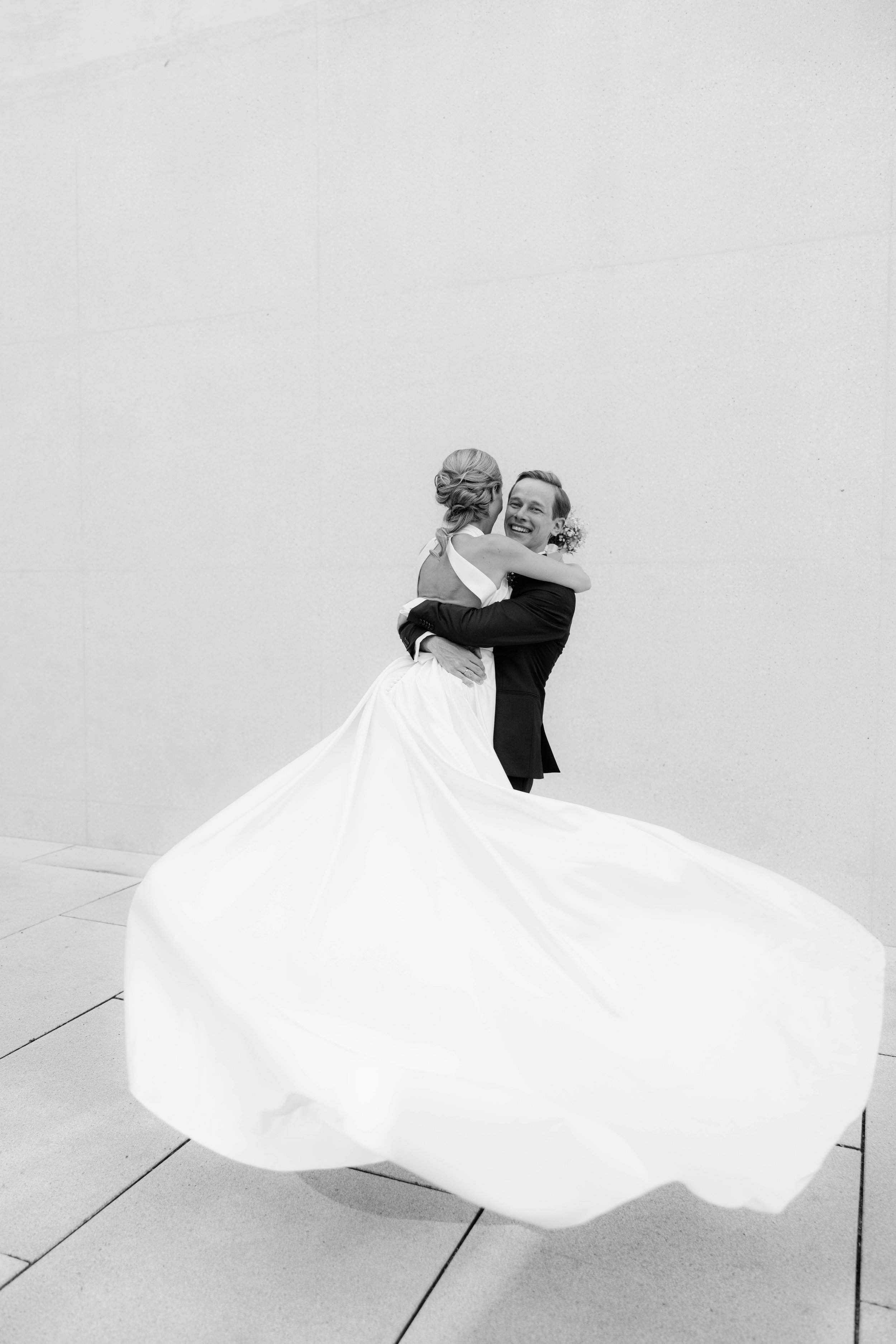 Ein glückliches Brautpaar, das sich umarmt, vor einer weißen Wand