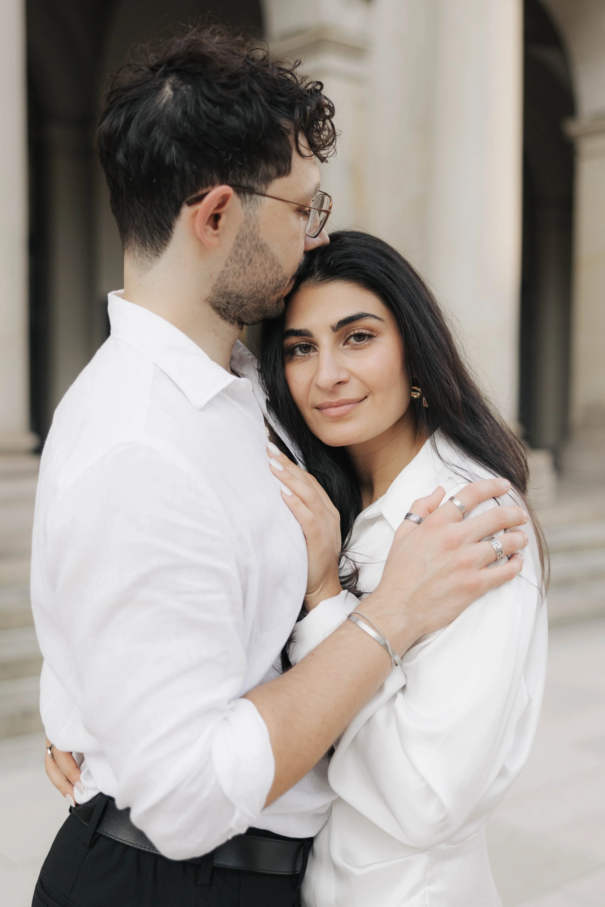 Ein Mann und eine Frau umarmen sich vor einer monumentalen Architektur im Hintergrund.
