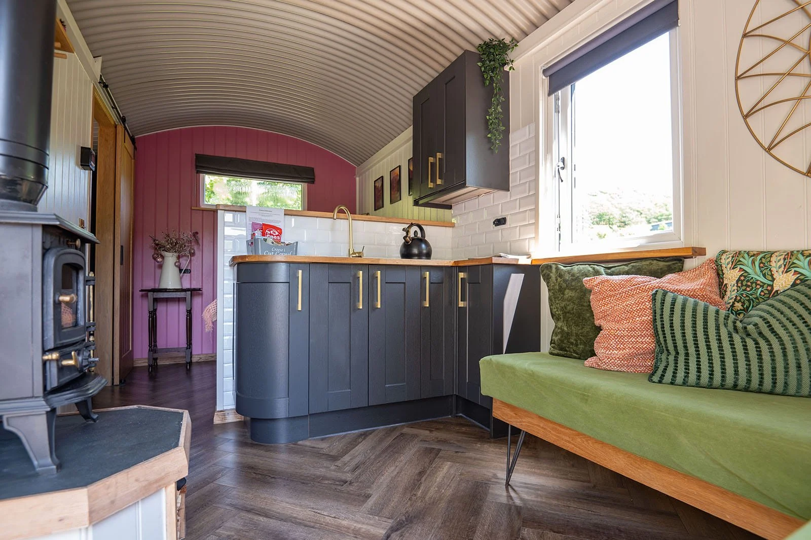 Interior of a cozy kitchen with dark cabinets, a green cushioned seating area, and a pink accent wall.