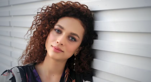 Woman with curly hair leaning against a slatted wall