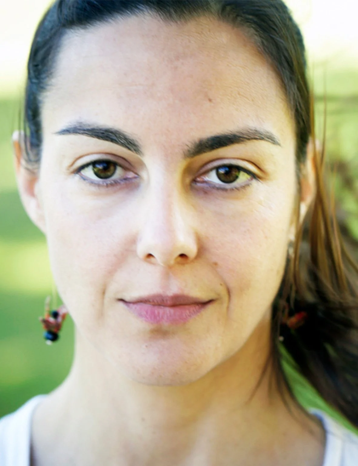 Close-up of a woman's face, neutral expression, wearing earrings, with blurred green background.