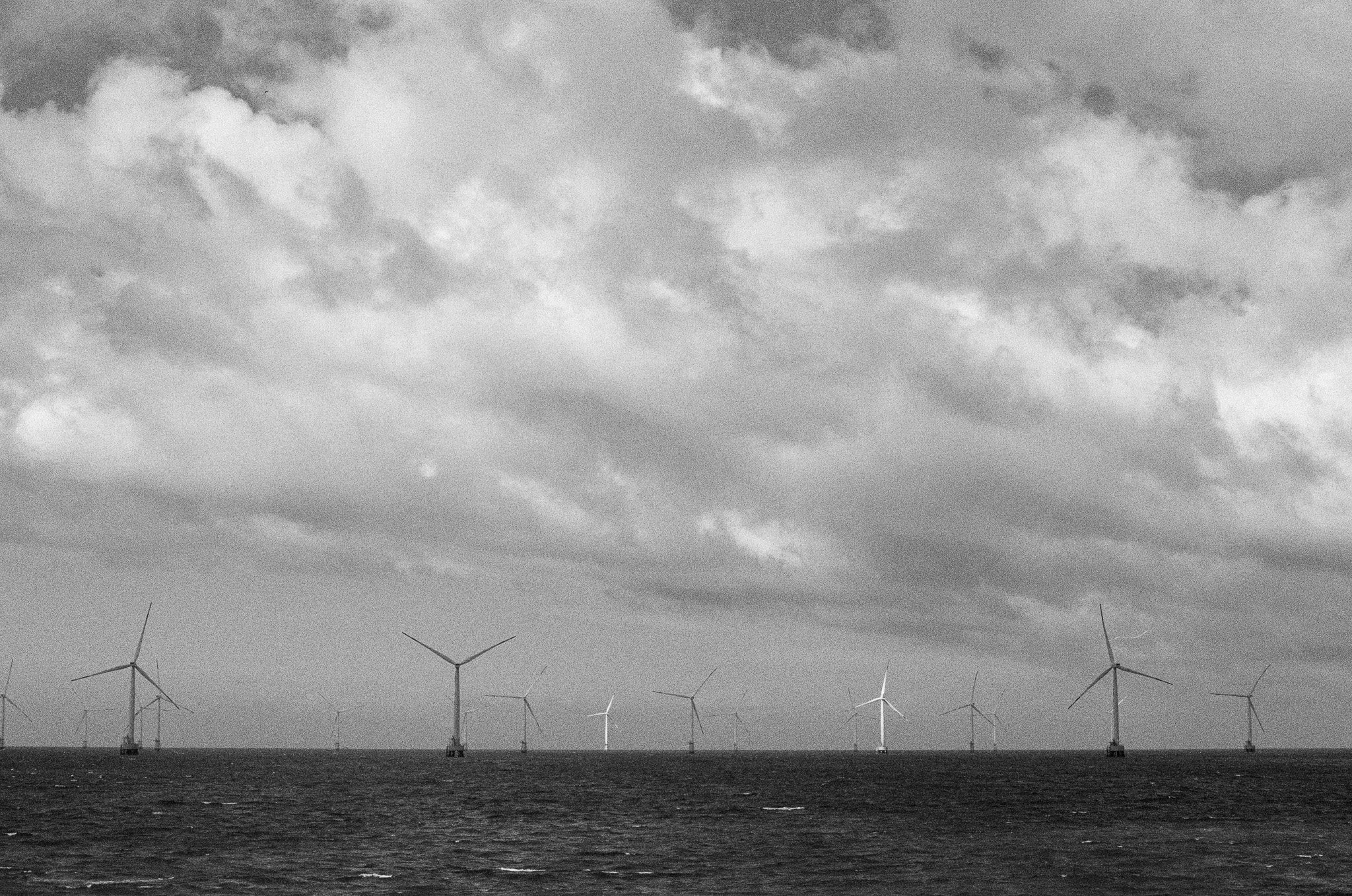 Offshore wind turbines in the ocean beneath a cloudy sky.