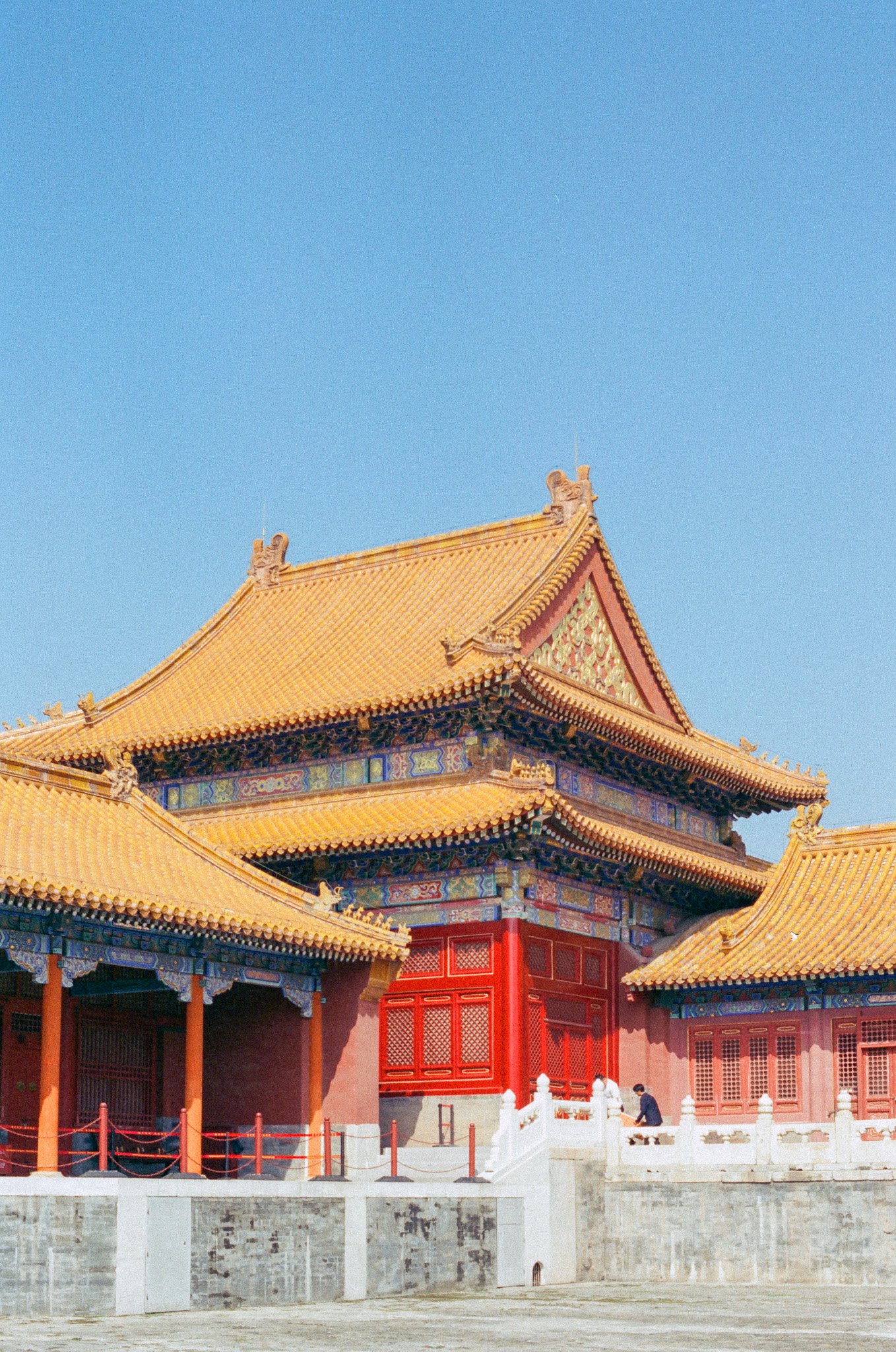 Traditional Chinese palace with yellow tiled roofs and red walls against a clear blue sky.