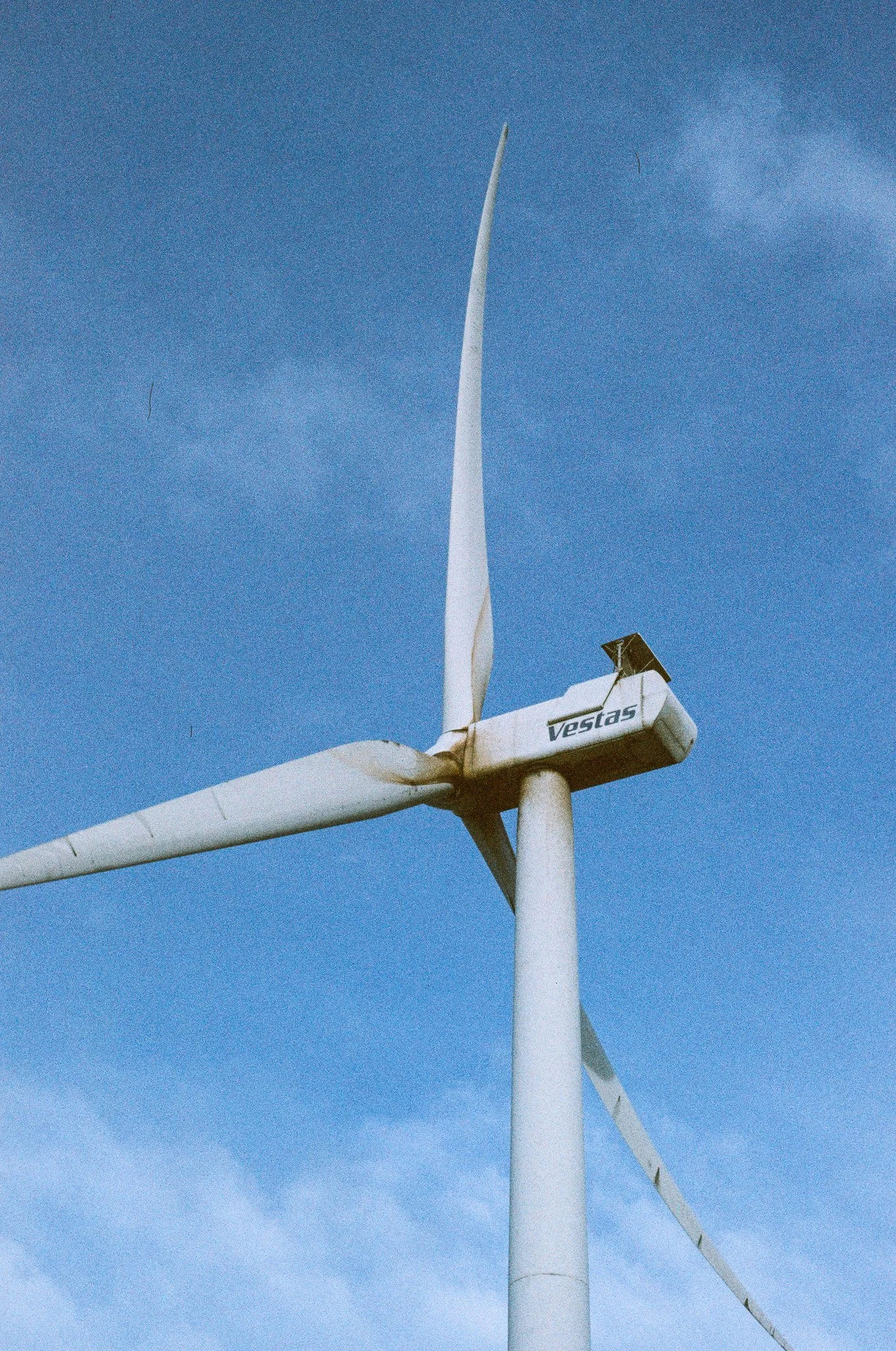 A large white wind turbine stands against a partly cloudy blue sky.