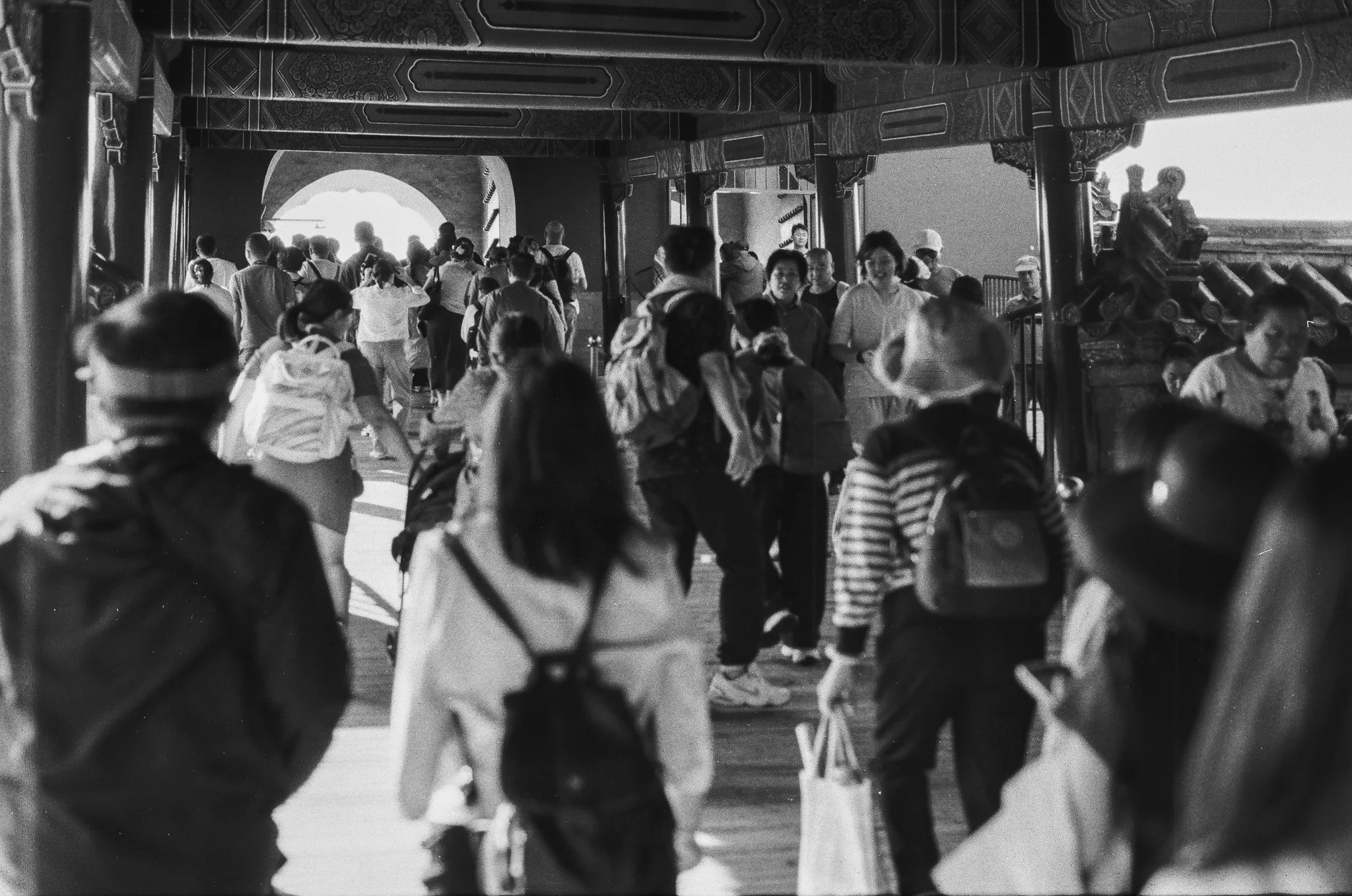 Crowded scene of many people walking through a traditional Asian architectural structure with ornate details and a cannon on the right.