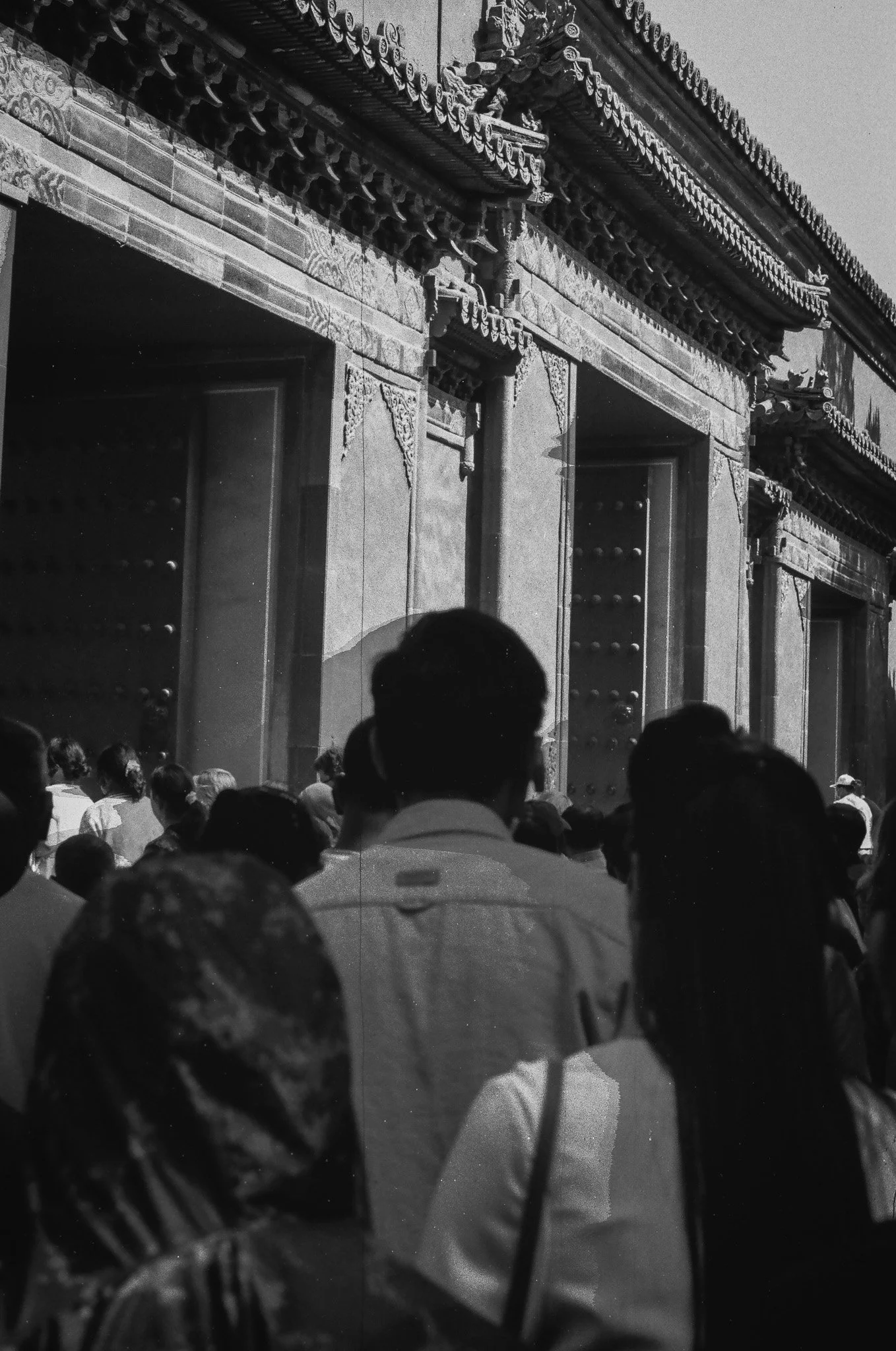 A crowd of people standing outside a traditional Chinese building with ornate architectural details, such as decorative eaves and large doors.