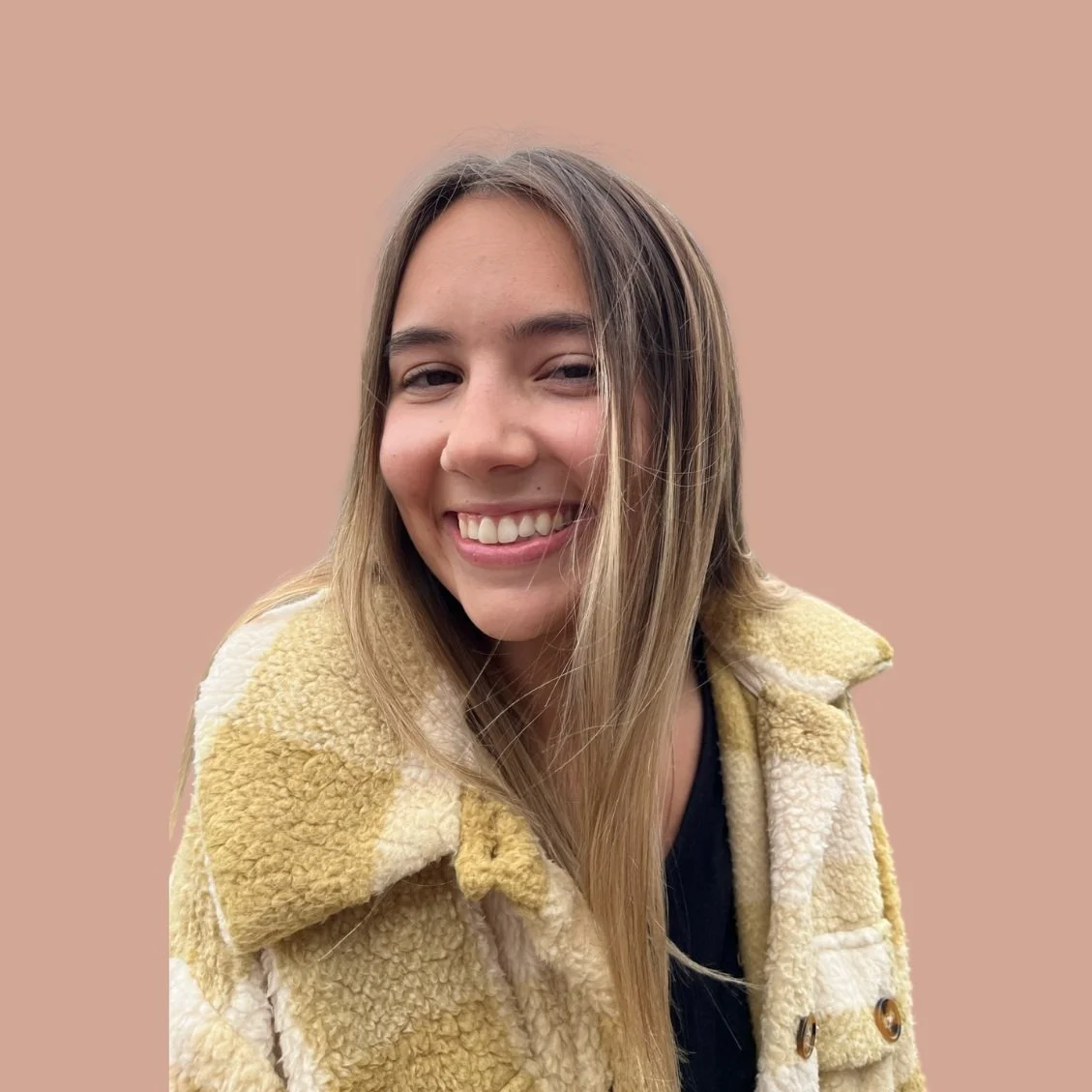 A young woman with long hair smiling, wearing a yellow and cream fuzzy jacket, against a plain beige background.