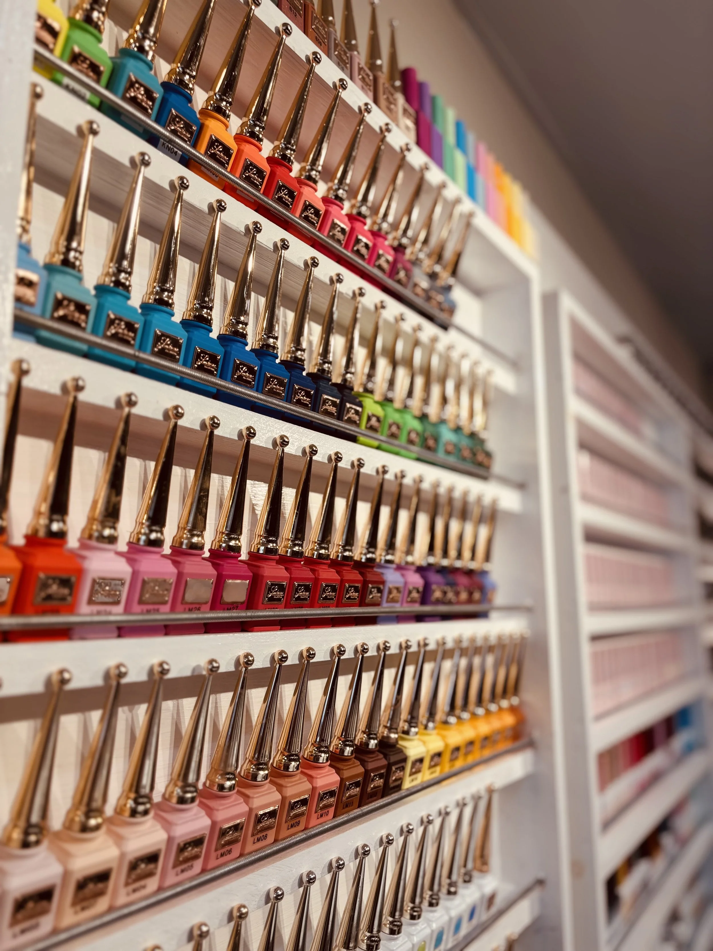 Shelves filled with colorful nail polish bottles with gold caps, organized by color.