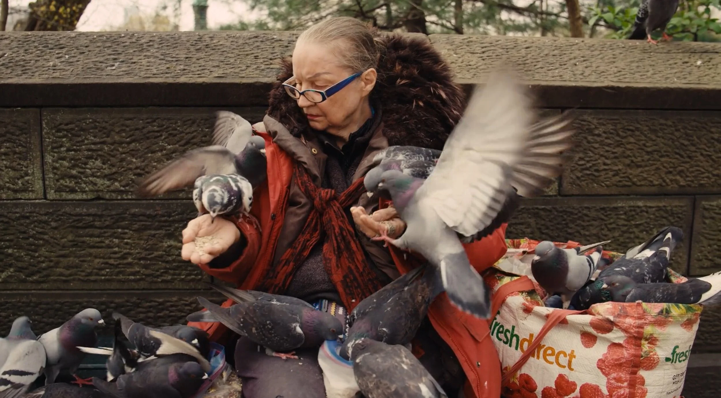 Woman feeding pigeons from her hands and a bag of birdseed outdoors.
