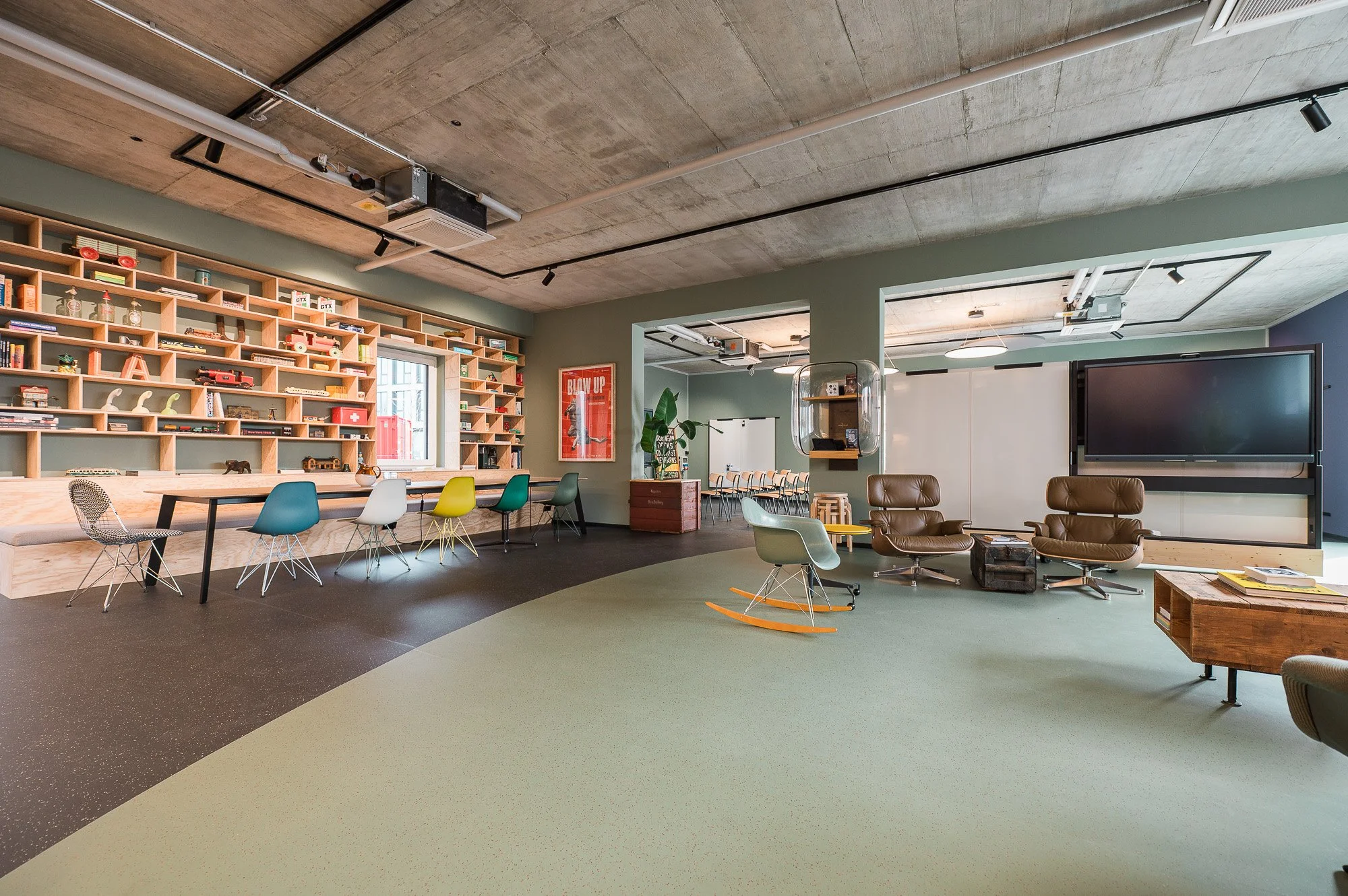 Ein moderner Loungebereich mit braunen und grauen Sesseln, einem kleinen Holztisch, einem kleinen weißen Tisch und einem Koffer, in dem Zeitschriften liegen.