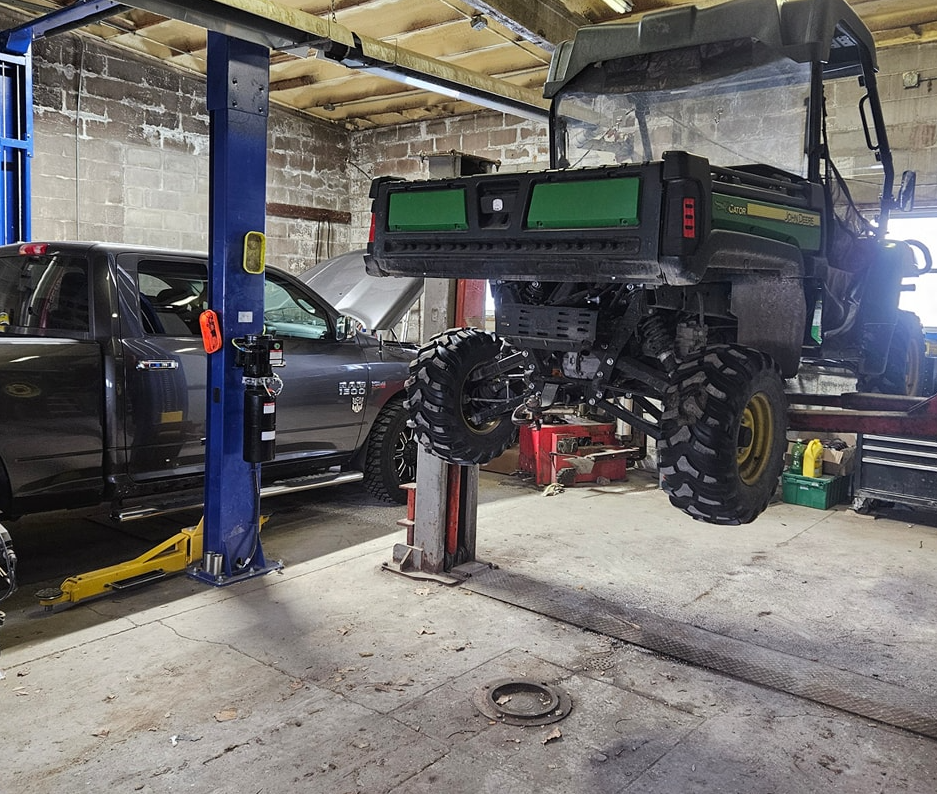 Workshop interior with an ATV on a lift and a pickup truck with hood open.