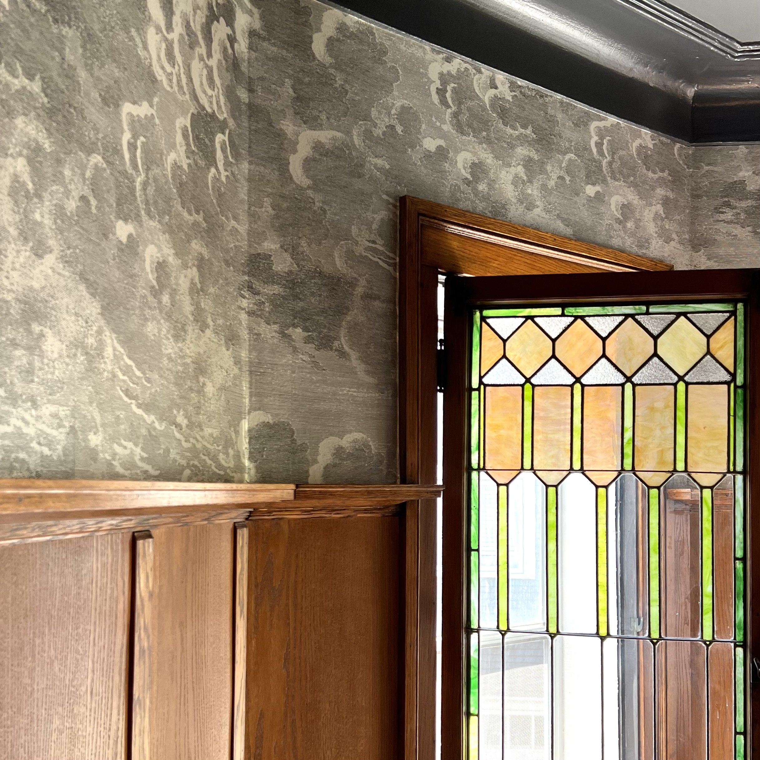 Interior showing stained glass window with a wooden frame, patterned wallpaper, and wainscoting on the wall.