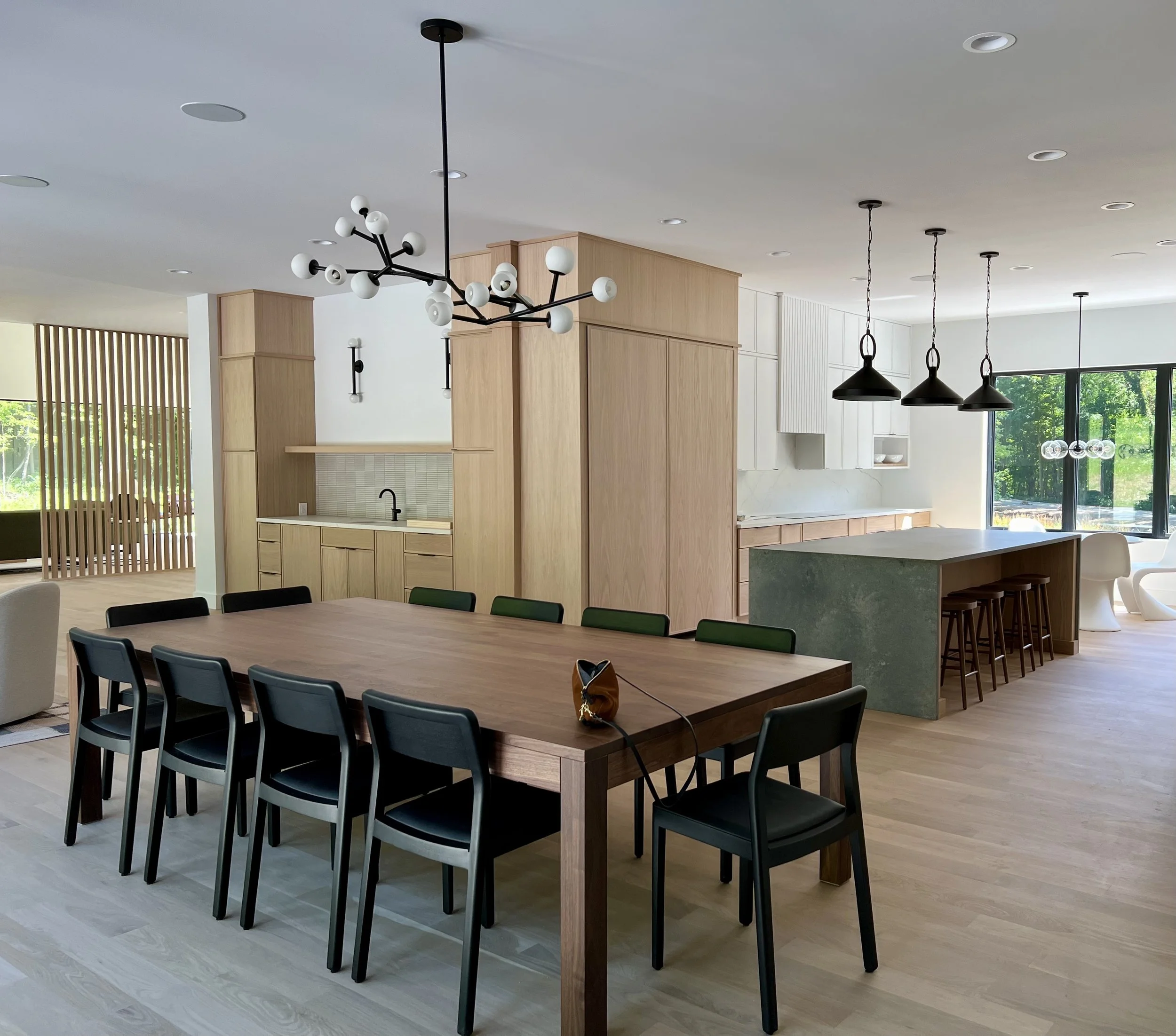 Modern kitchen and dining area with wooden table, black chairs, pendant lighting, and a kitchen island with bar stools.