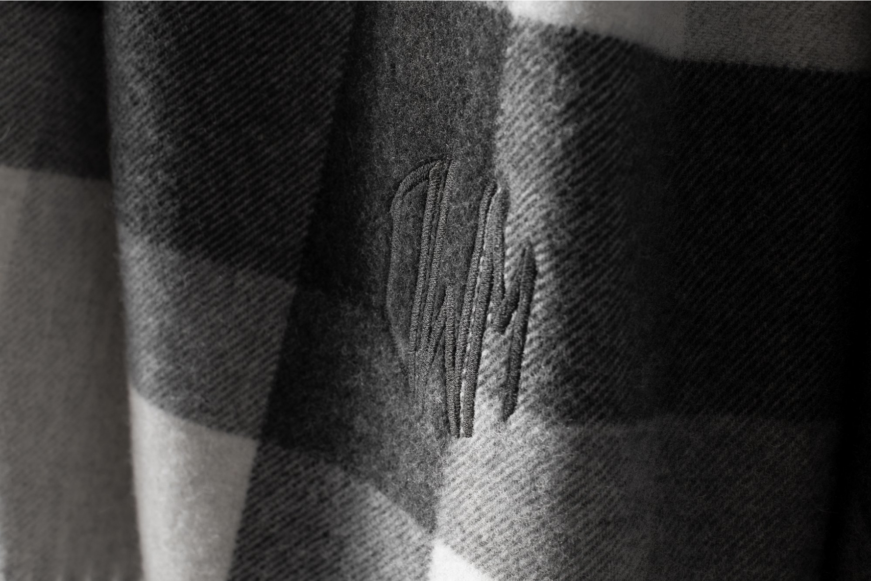 Close-up of a fabric with a stitched logo or embroidery, featuring a checkered pattern in shades of gray and black.