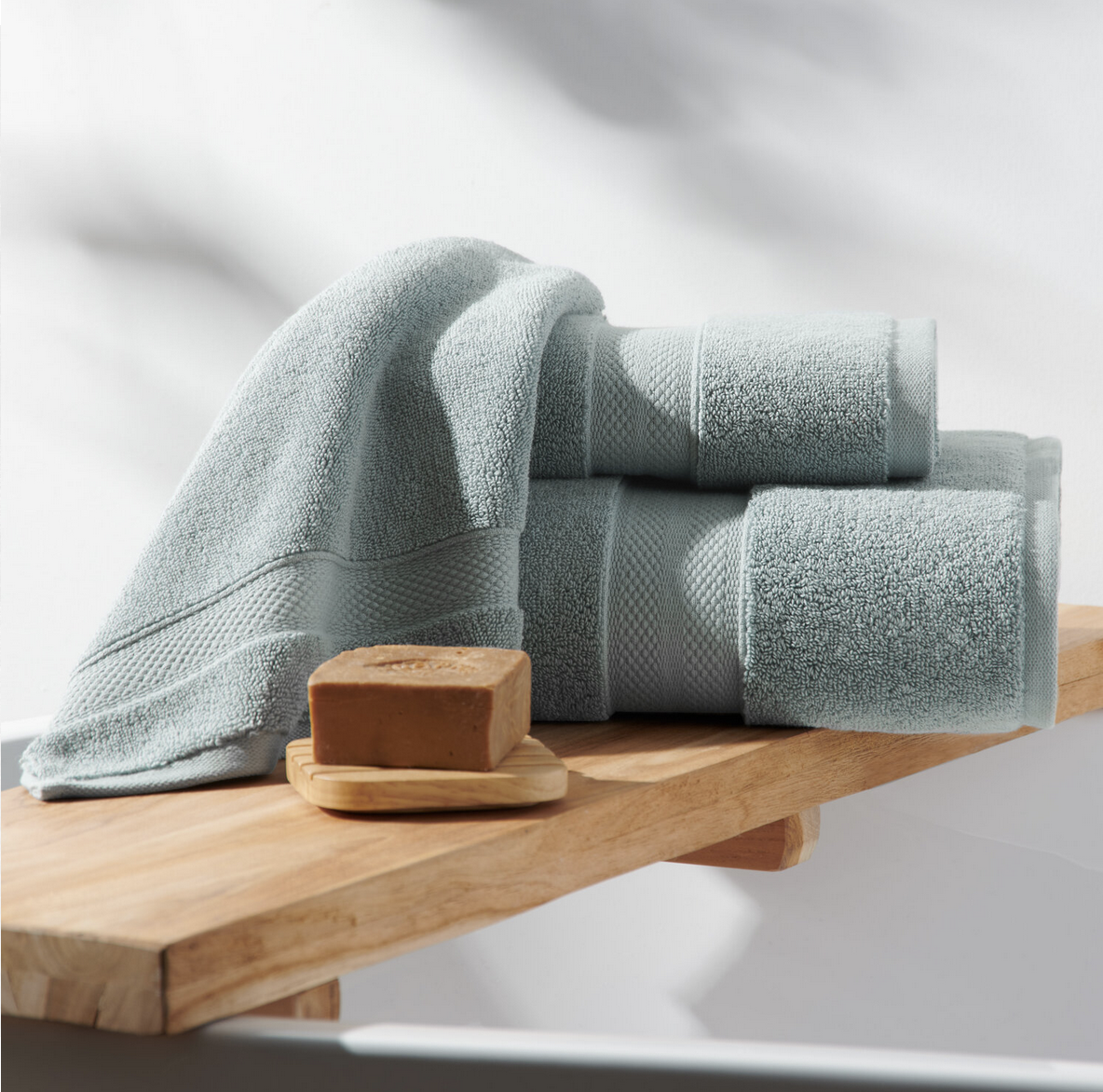 Three folded light blue towels stacked on a wooden surface with a bar of soap on a small wooden dish in front of them.