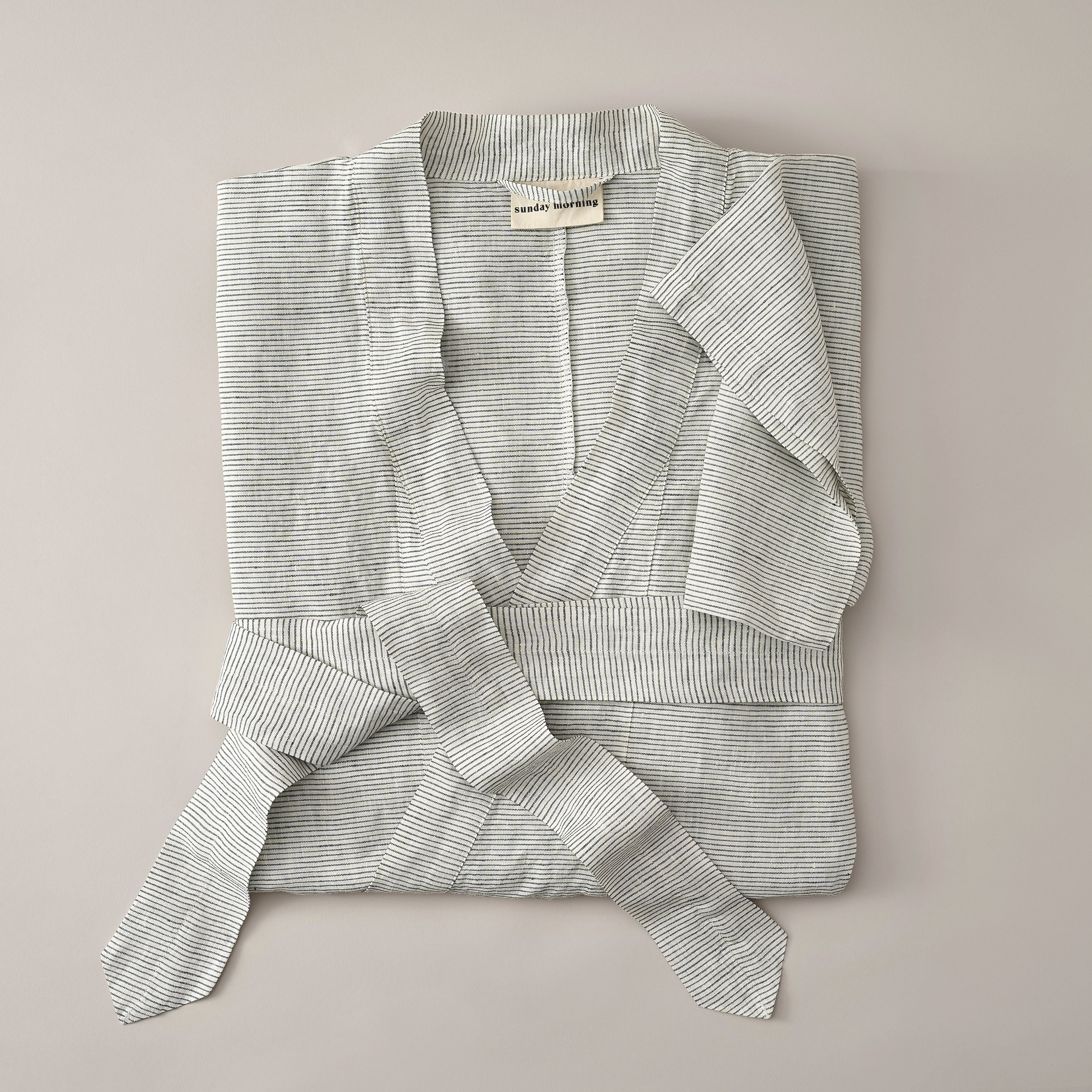 A folded shirt with thin black and white stripes laid out on a light-colored surface.