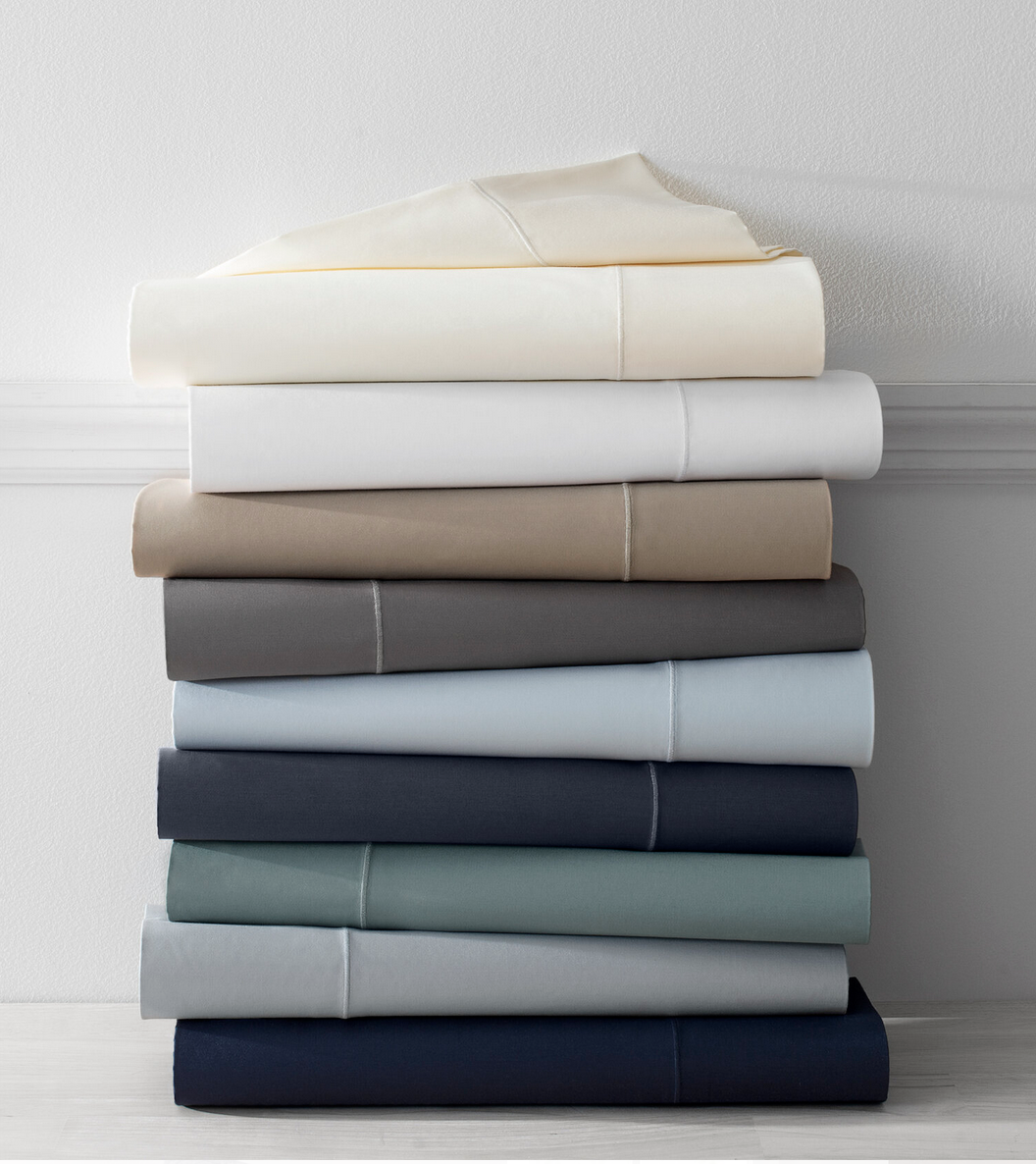 Stack of folded bedsheets in various colors against a white wall.