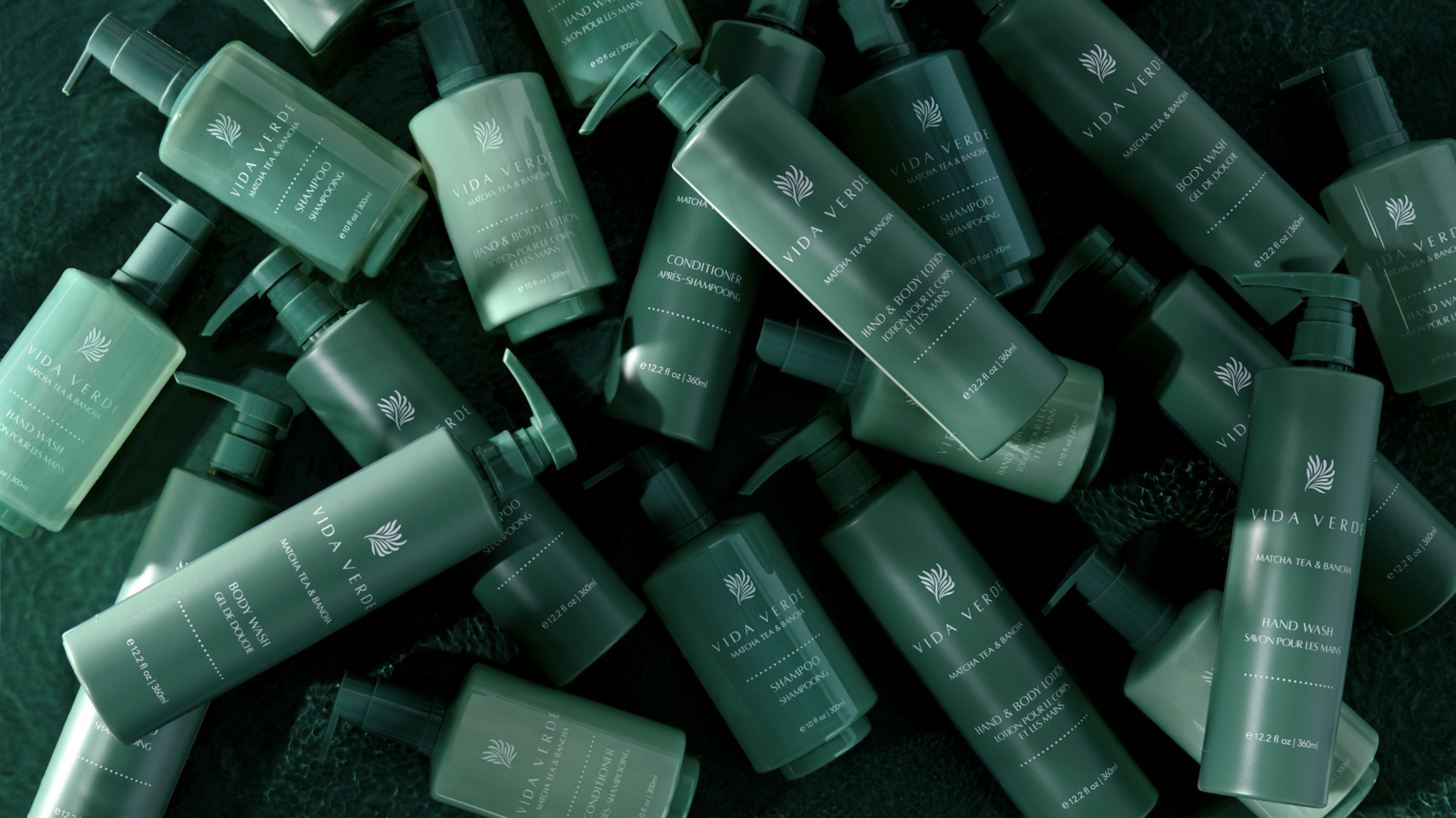 Multiple green bottles of Vida Verde bath and body products, including shampoo, conditioner, hand wash, and body lotion, scattered on a dark textured surface.