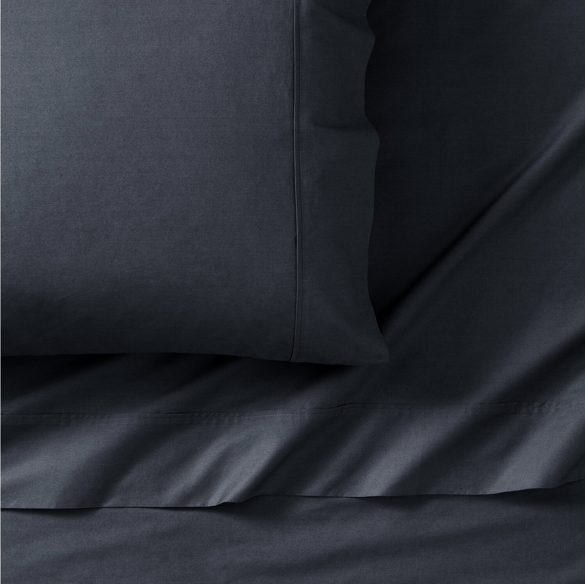 Close-up photo of a dark gray pillow and bed sheets made of smooth fabric.