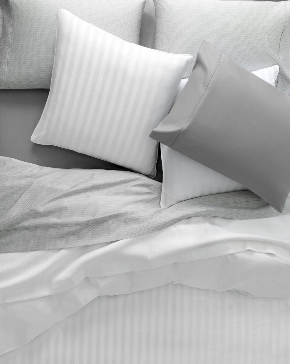A neatly made bed with multiple pillows in shades of white and gray.