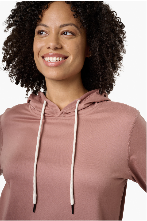 Close-up of a smiling young woman with curly hair wearing a pink hoodie with white drawstrings. She is looking slightly to her left.