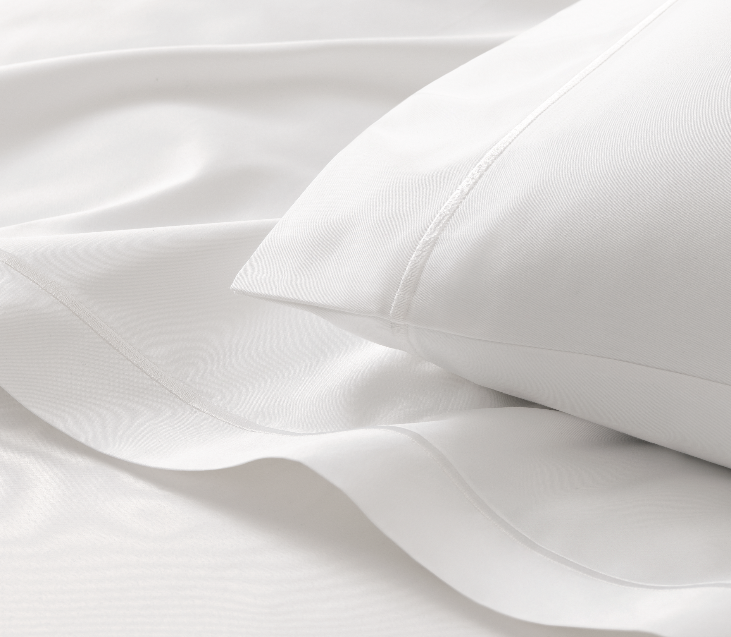 Close-up of white satin bedsheets and a pillow.