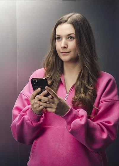 Junge Frau in pinkem Pullover benutzt Smartphone in Dunkelheit