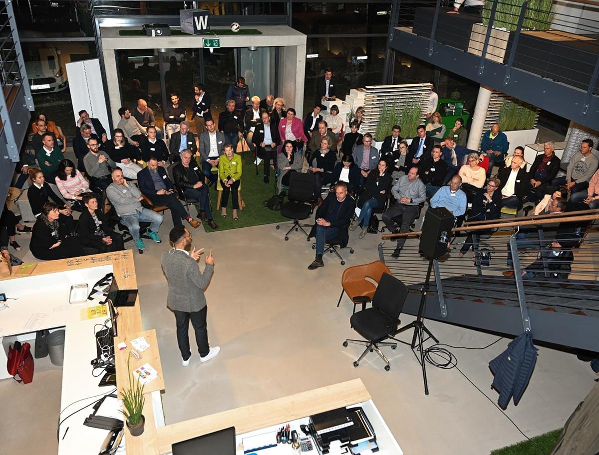 Ein Mann hält eine Präsentation vor einem Publikum in einem modernen Büro oder Veranstaltungsraum.