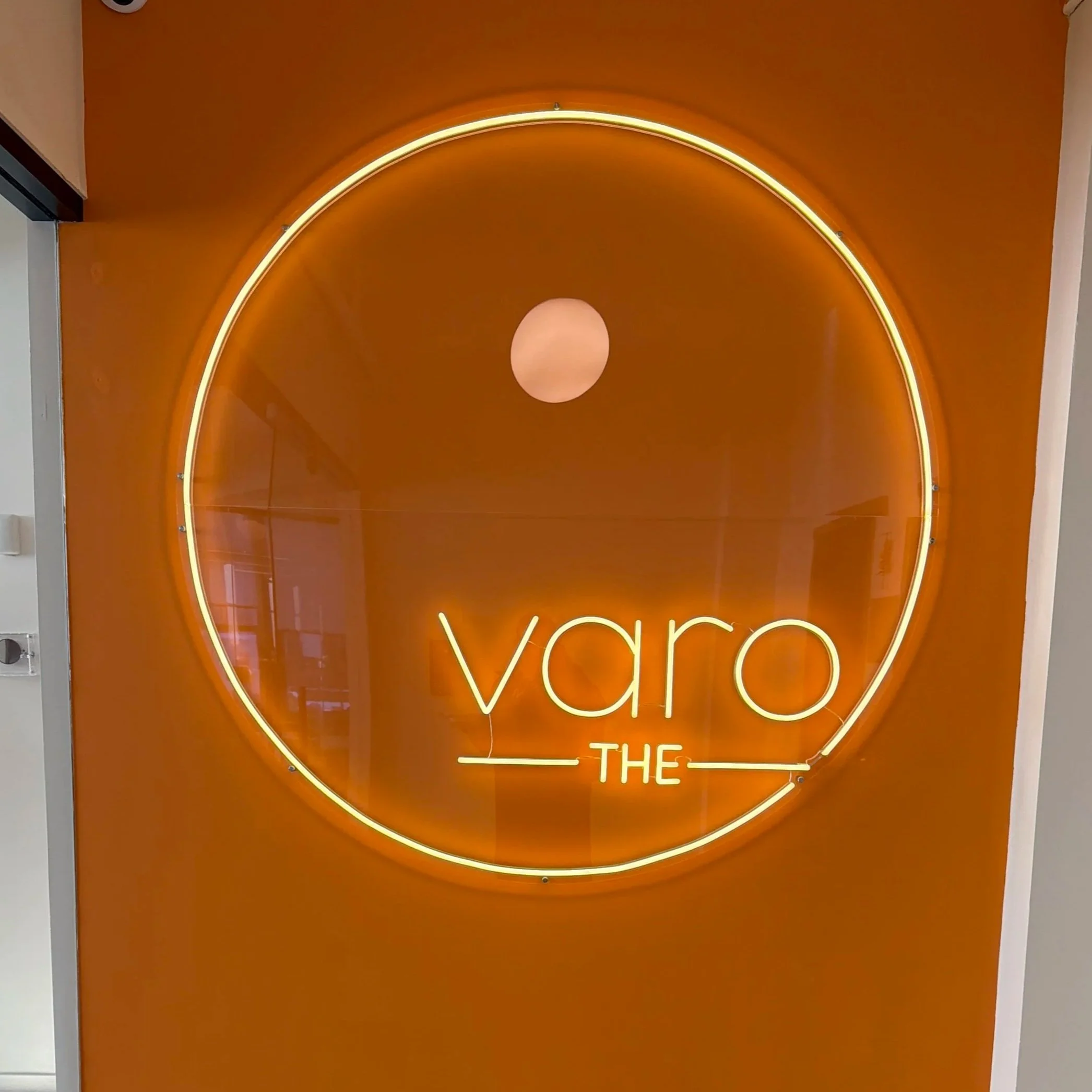 Neon sign with the words "varo THE" inside a large orange circle on an orange wall